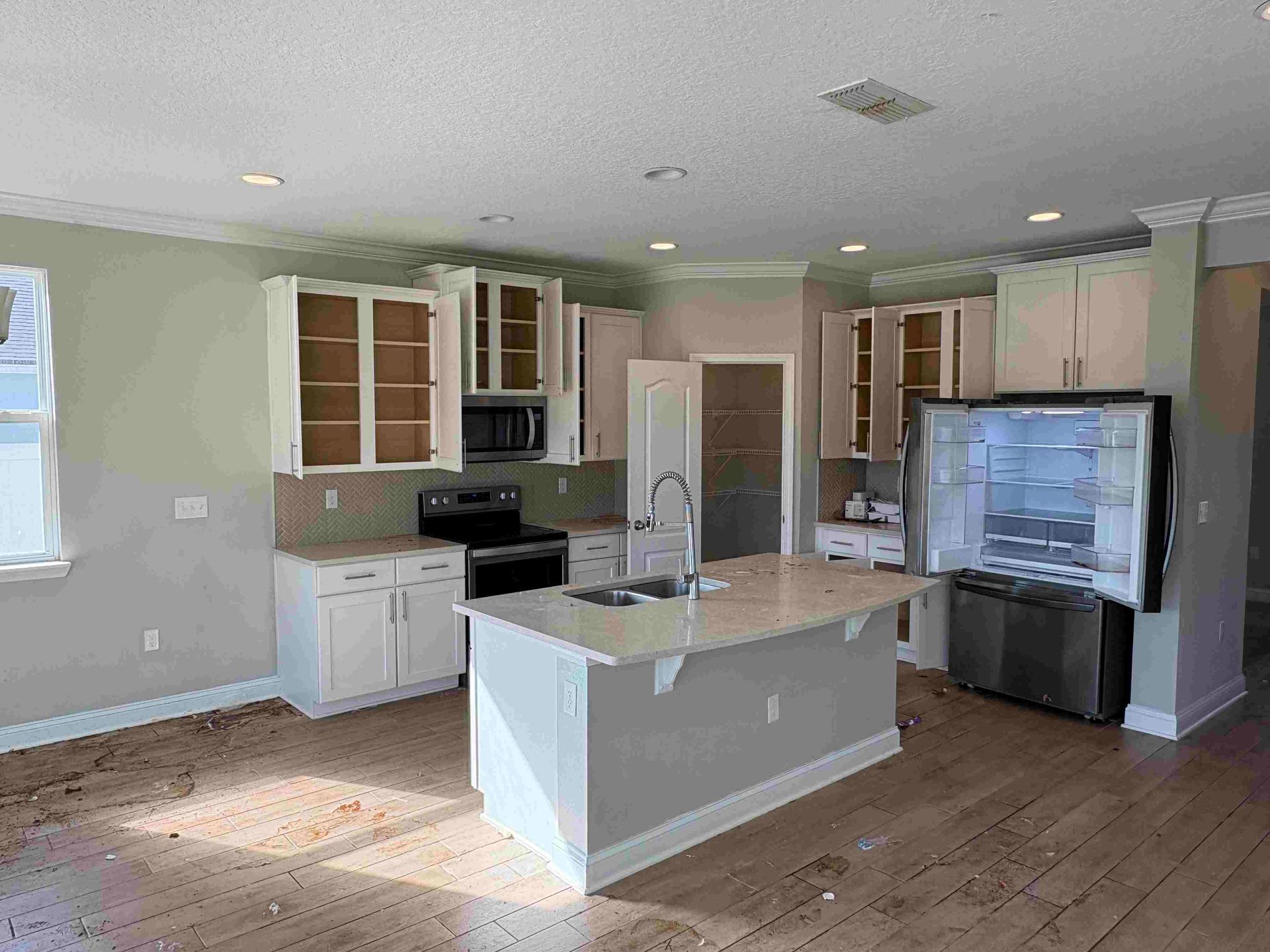 Kitchen with white cabinets, island, and stainless steel appliances. Hardwood floors and pale green walls.
