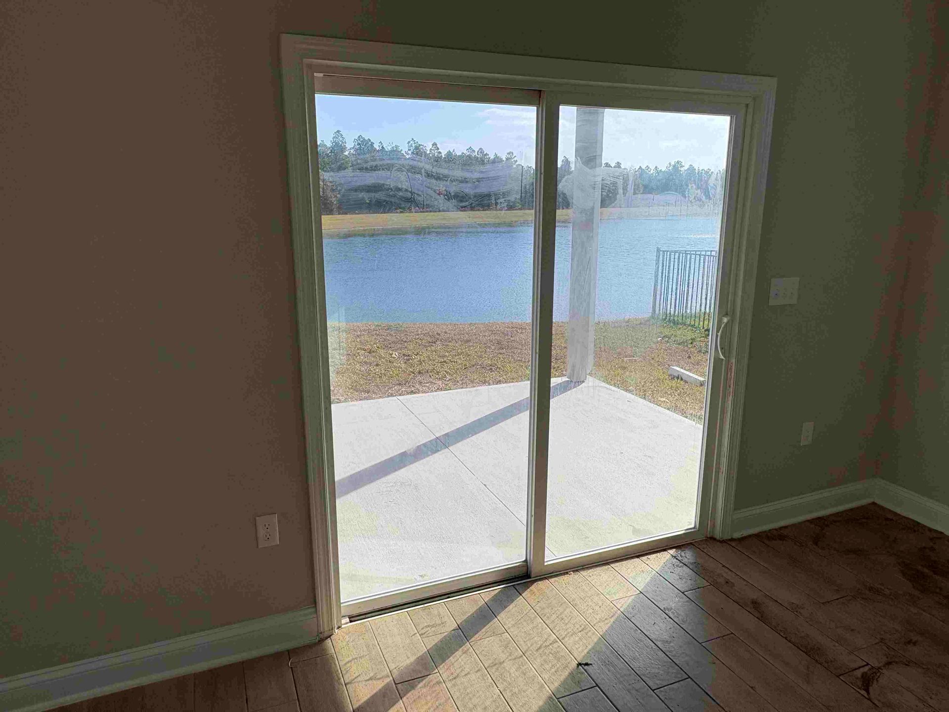 Sliding glass door opens to a lake view. Interior has light-colored walls and wood floors. Sunlight streams in.