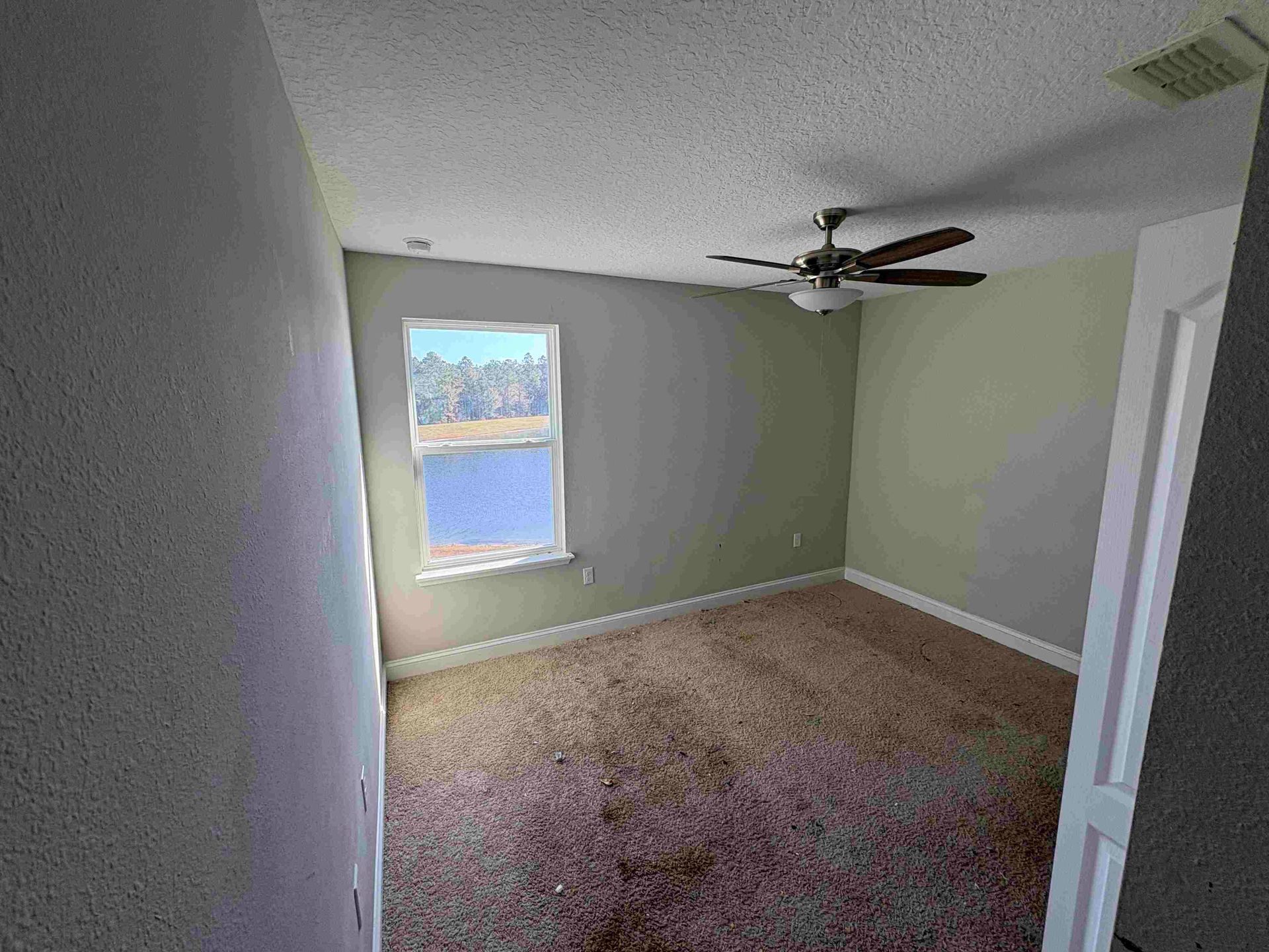 Empty bedroom with a window overlooking water, ceiling fan, and brown carpet.