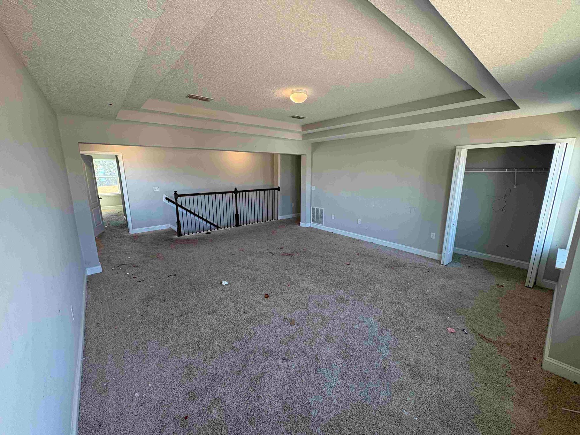 Empty room with carpet, recessed ceiling, closet, and stairs in the back.