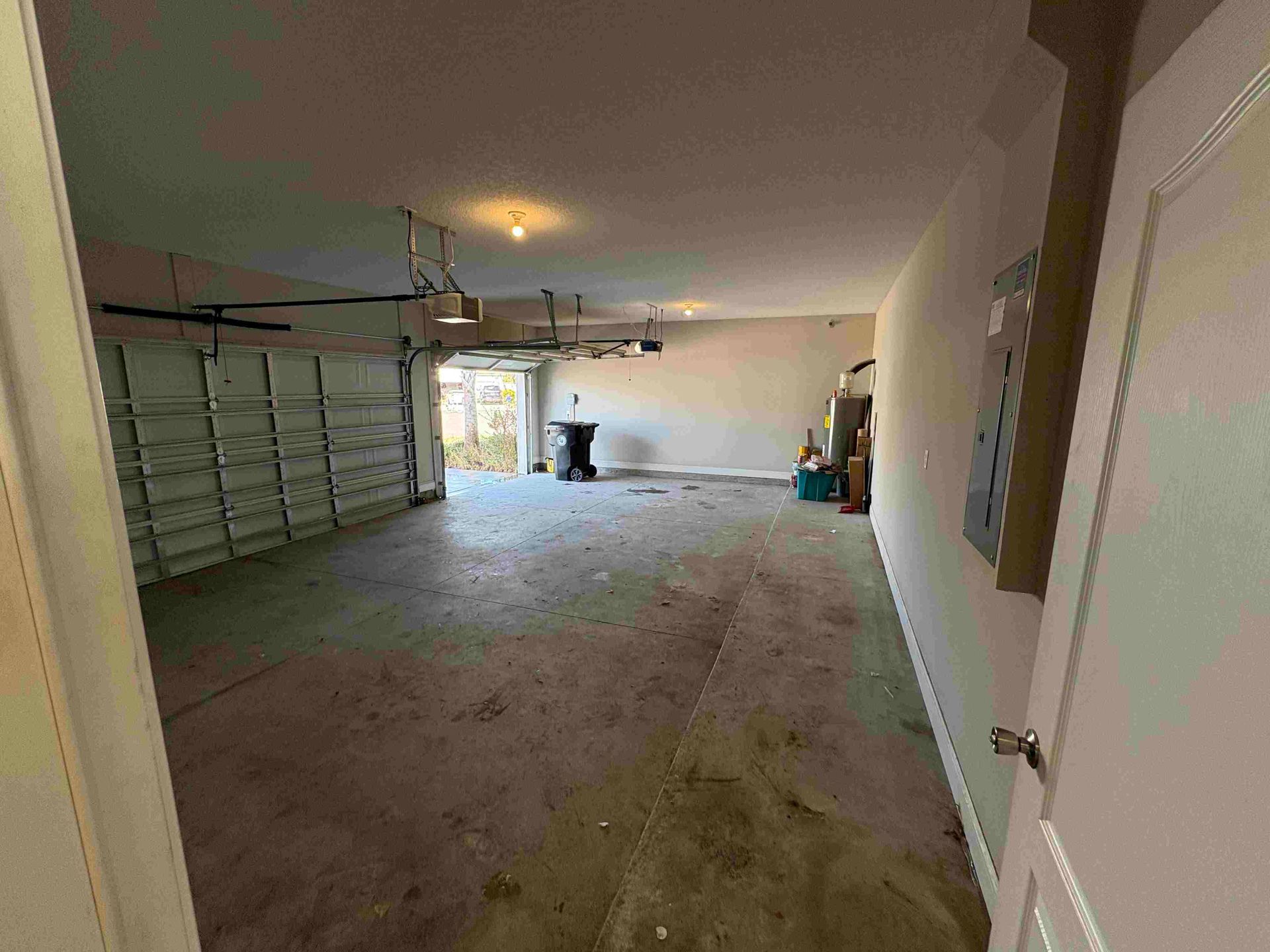 Empty garage with a gray concrete floor, garage door open, and door leading inside on the right.