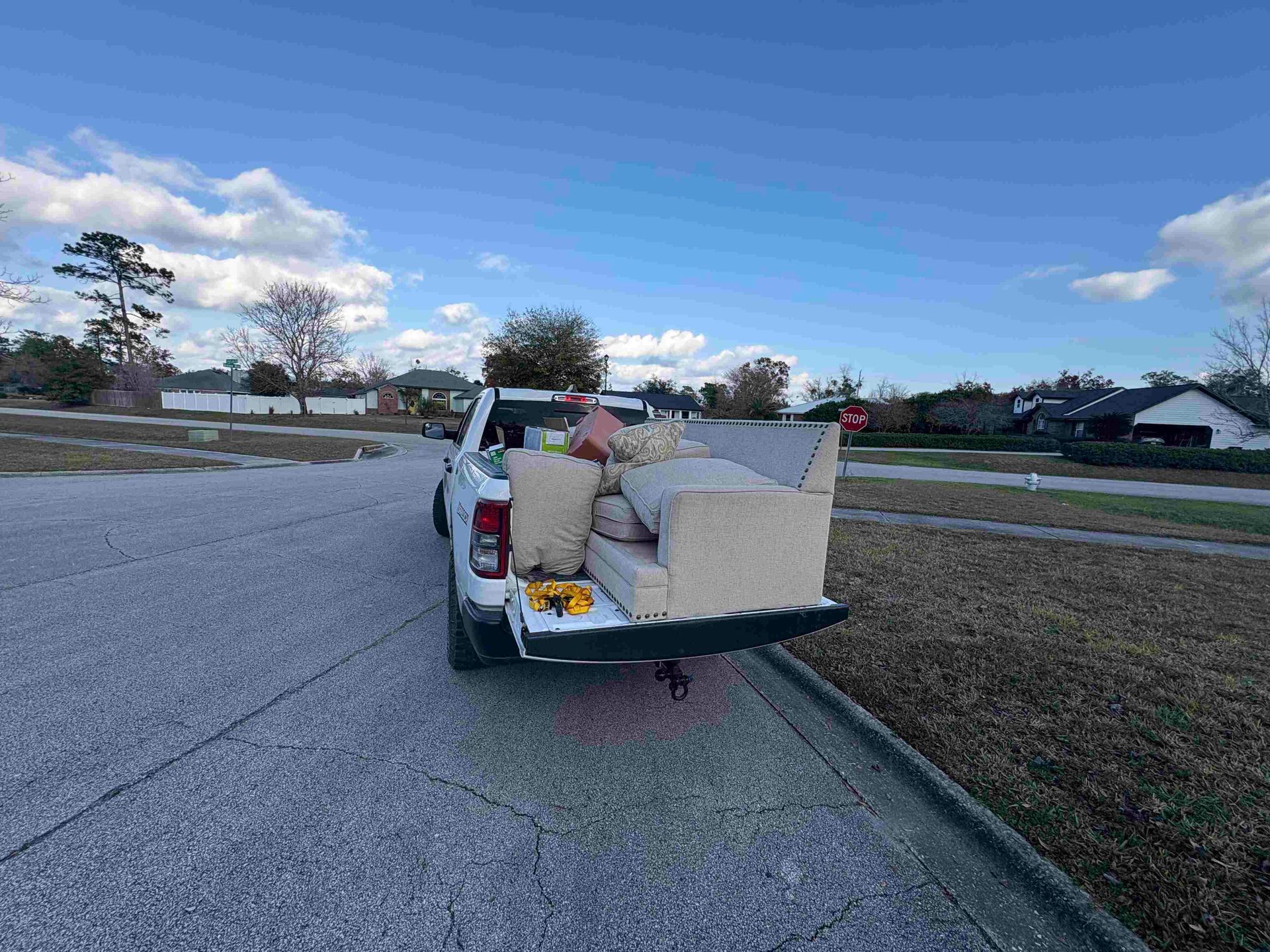 White pickup truck bed filled with furniture on a paved area, blue sky background.