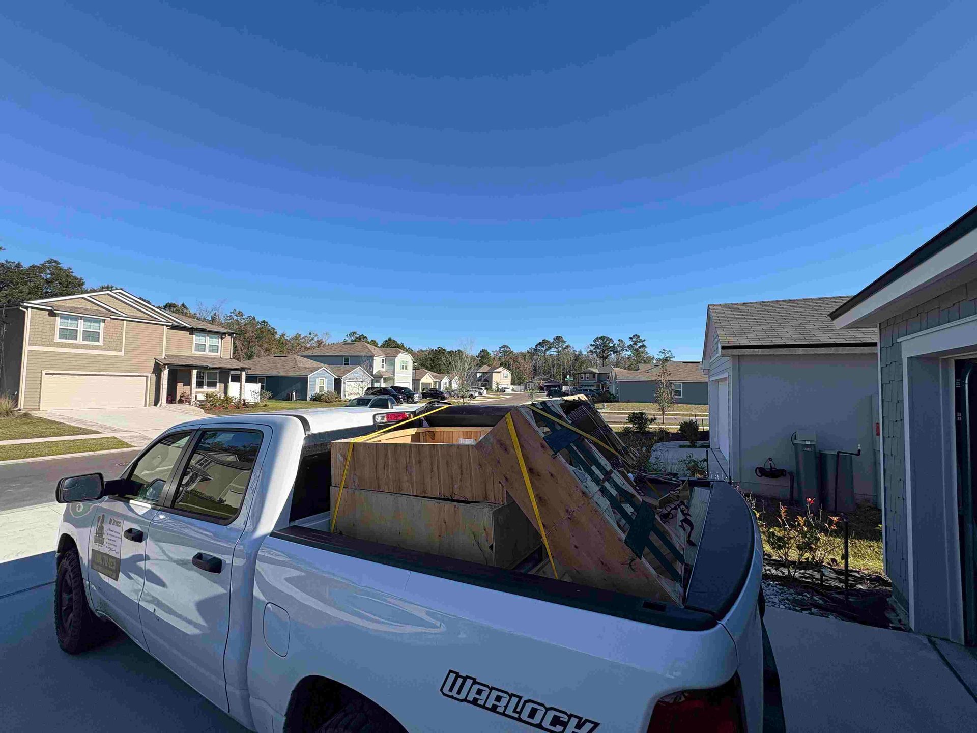 White pickup truck loaded with lumber in a suburban neighborhood on a sunny day.