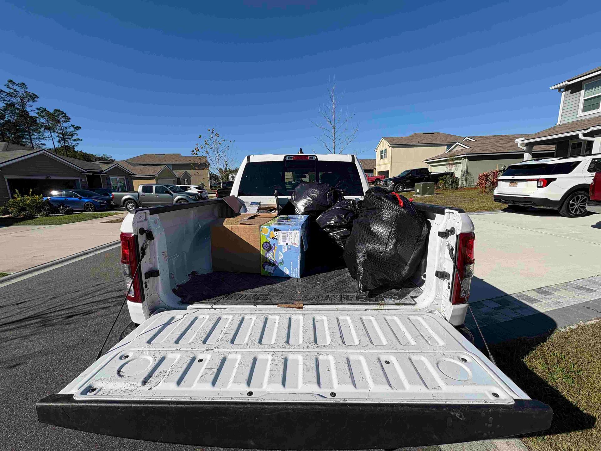 White pickup truck bed filled with items, tailgate down, houses in background under a blue sky.