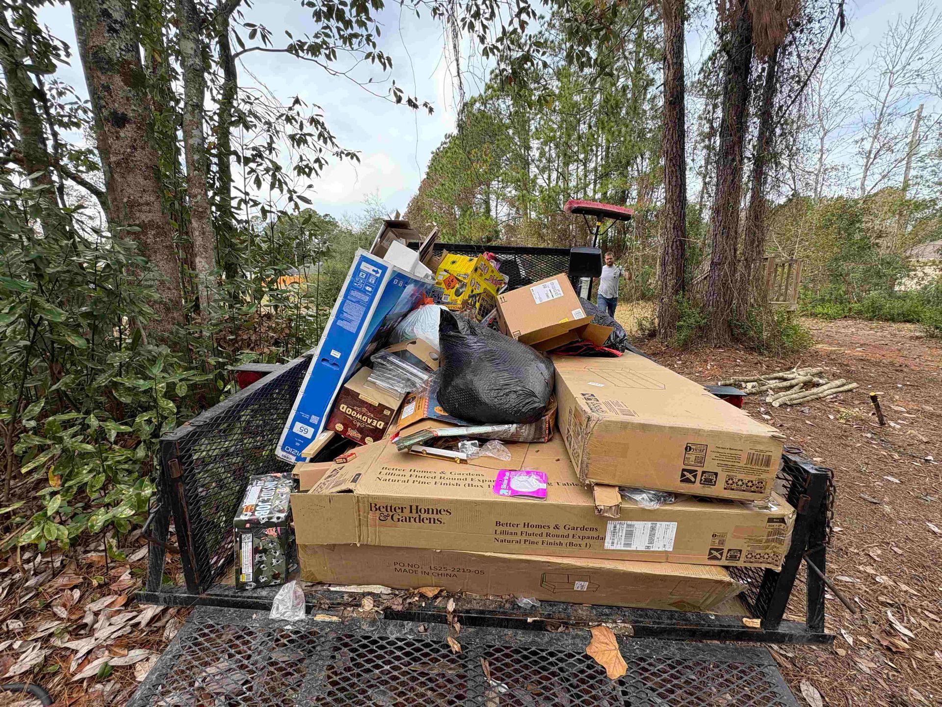A trailer filled with discarded cardboard boxes, trash bags, and other waste in an outdoor setting.