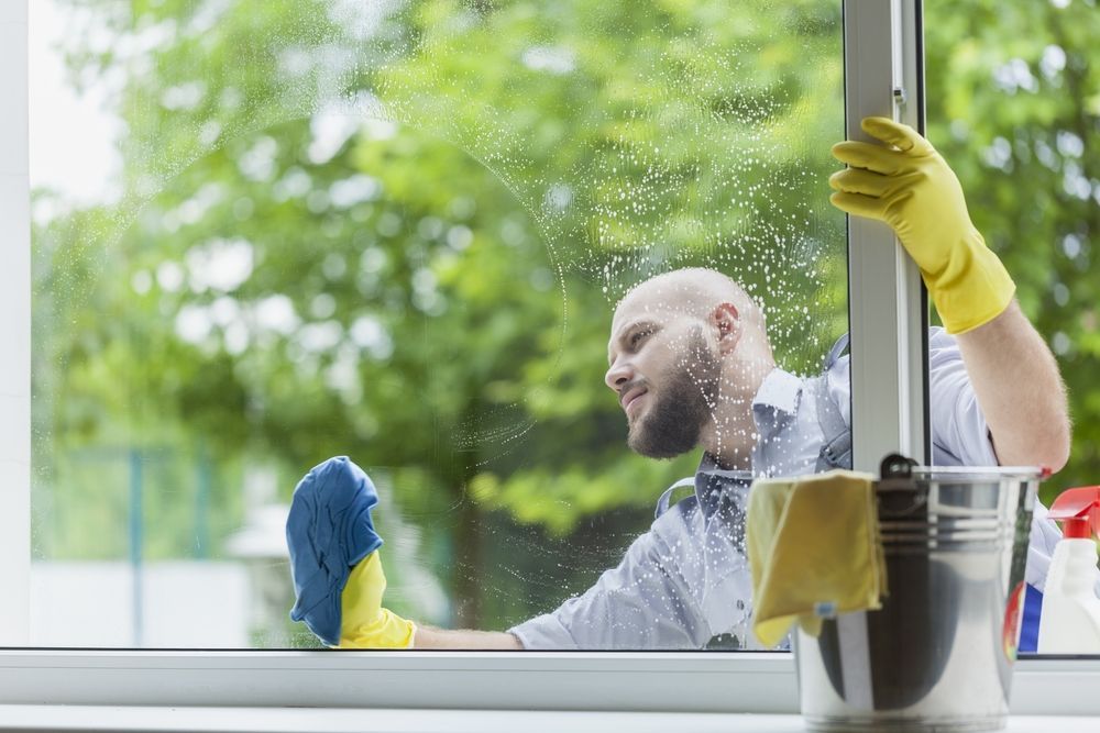 A Man is Cleaning a Window With a Cloth and Gloves — First Choice Cleaning Services in Wodonga, VIC