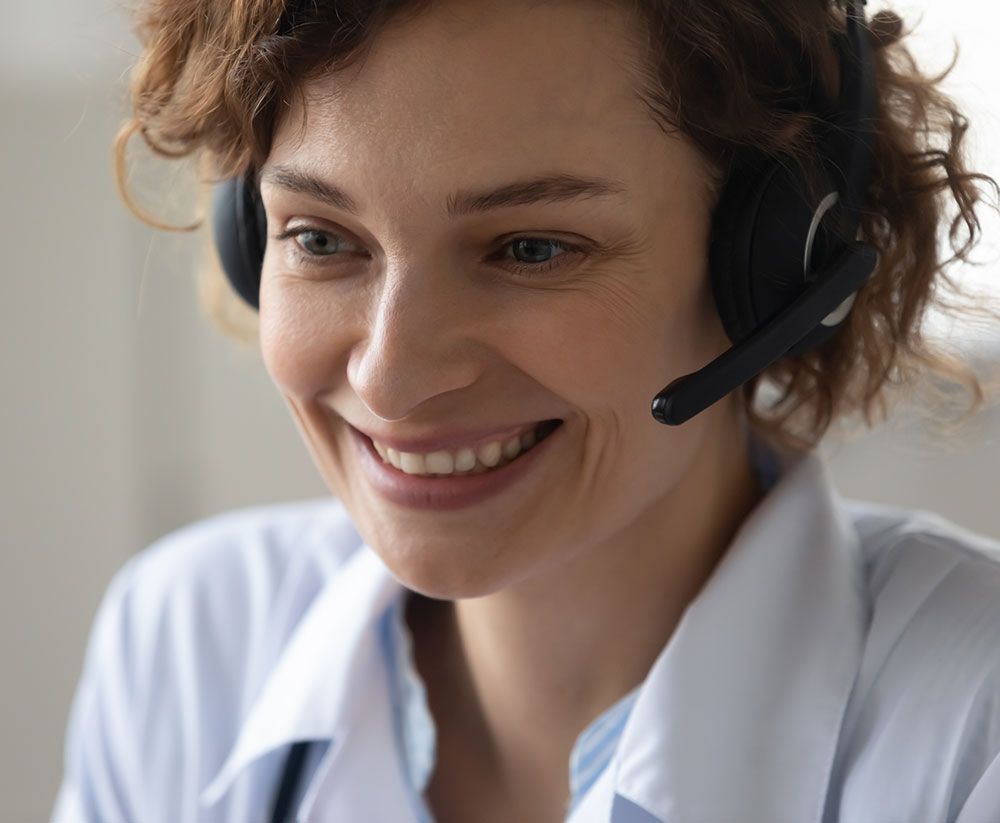 Woman with headset smiles while on a call; wearing a light blue shirt.