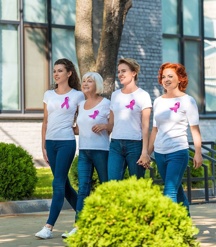 Four women in white t-shirts with pink ribbons and jeans walk together, supporting breast cancer awareness.