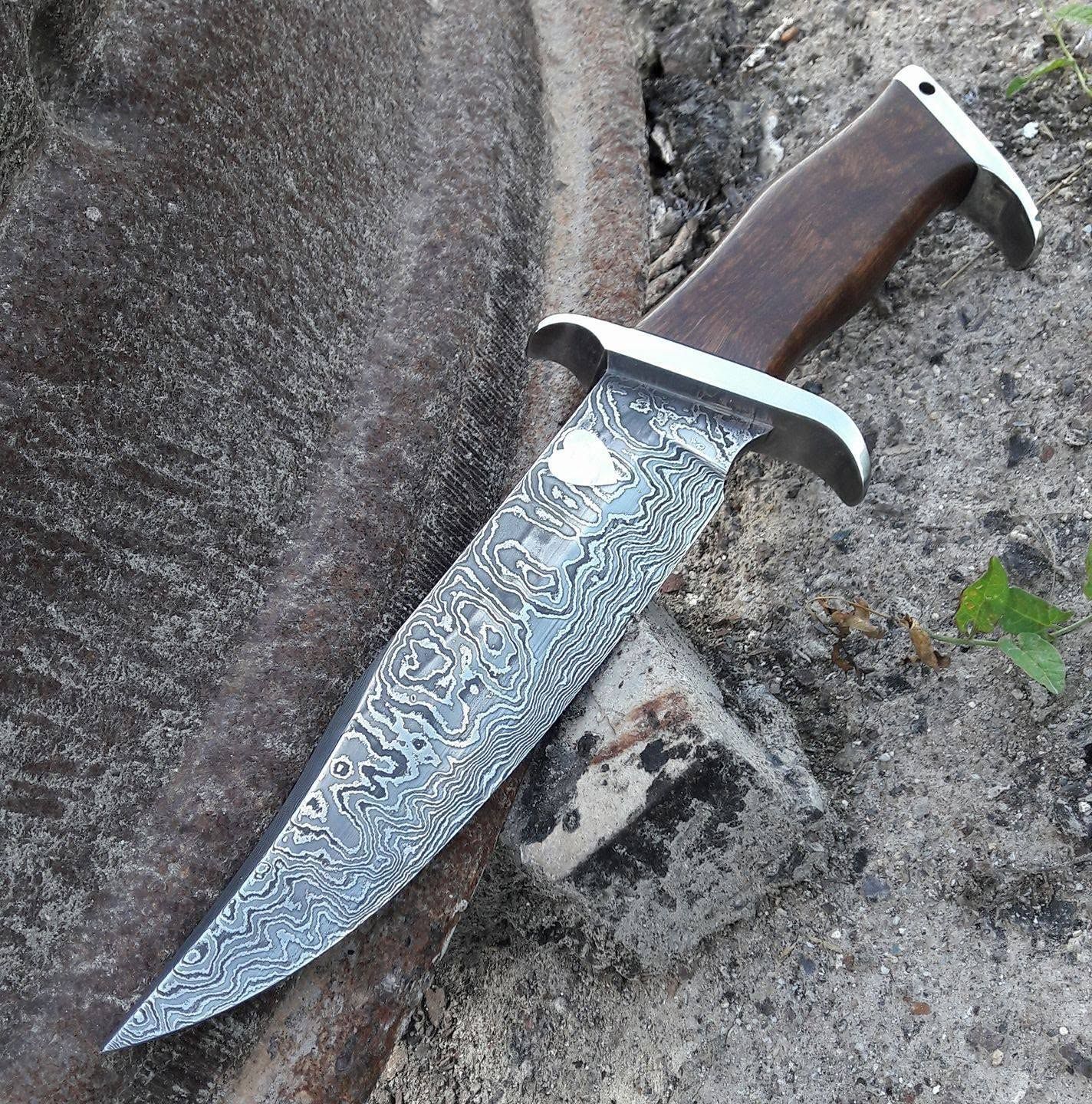 Damascus-style hunting knife with wooden handle resting on a rock outdoors