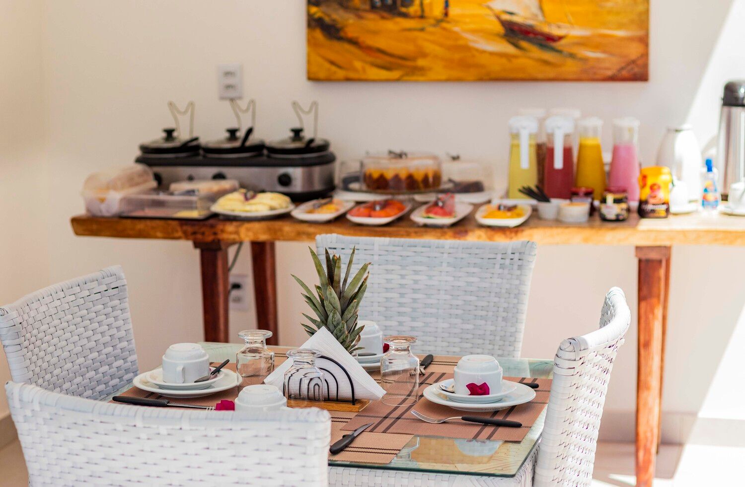 Uma mesa com pratos, xícaras, utensílios e um abacaxi.