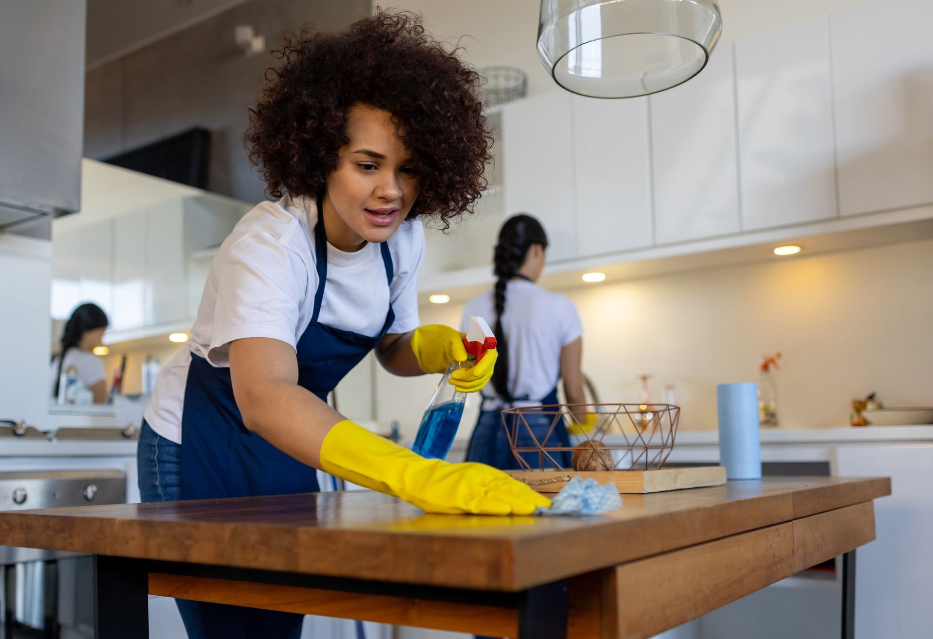 A woman is cleaning a wooden table in a kitchen.