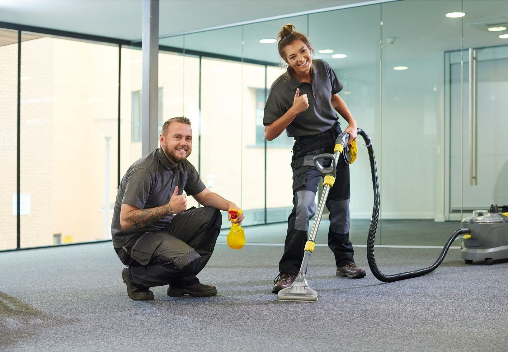A man and a woman are cleaning a carpet in an office.