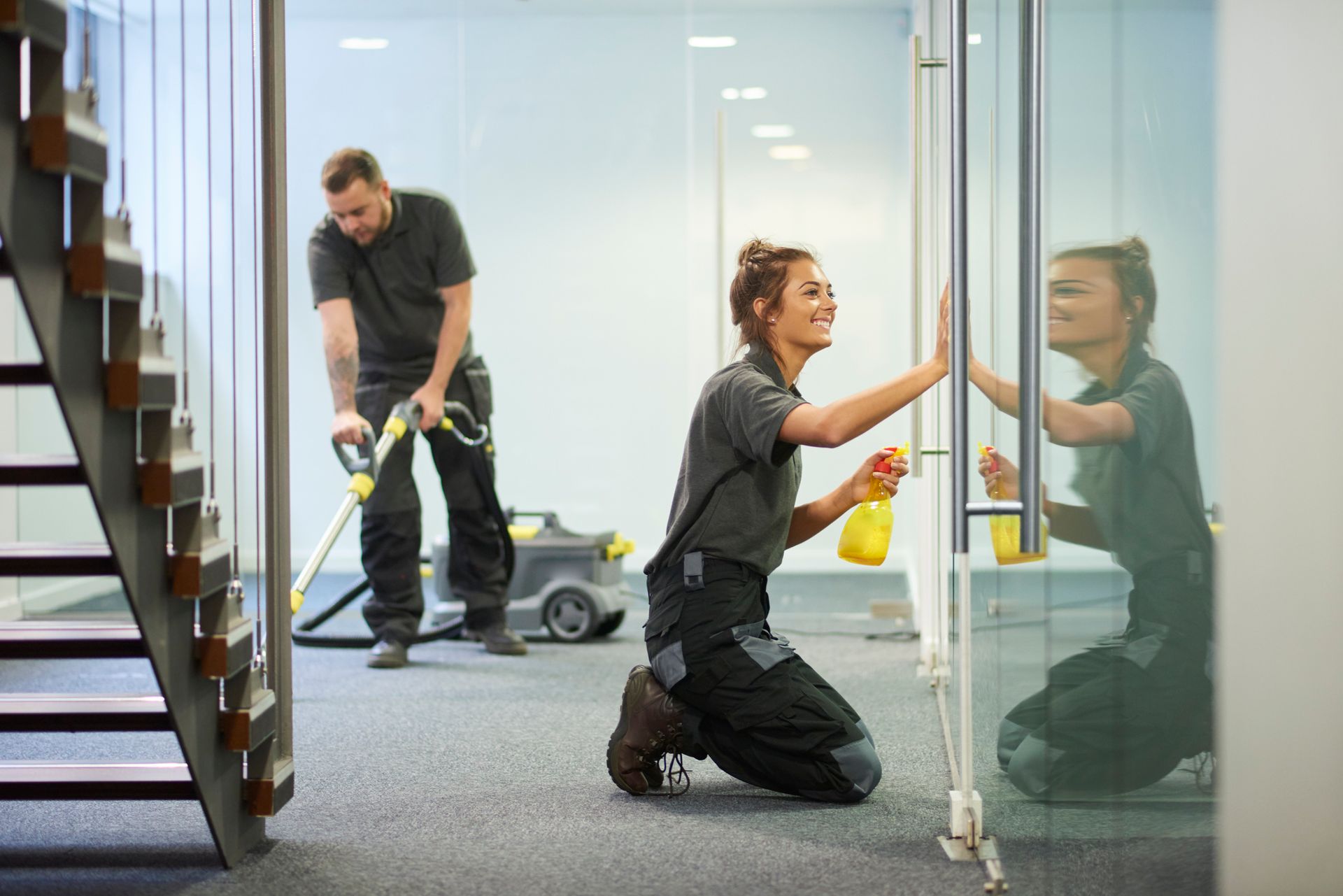 A man and a woman are cleaning an office with a vacuum cleaner.