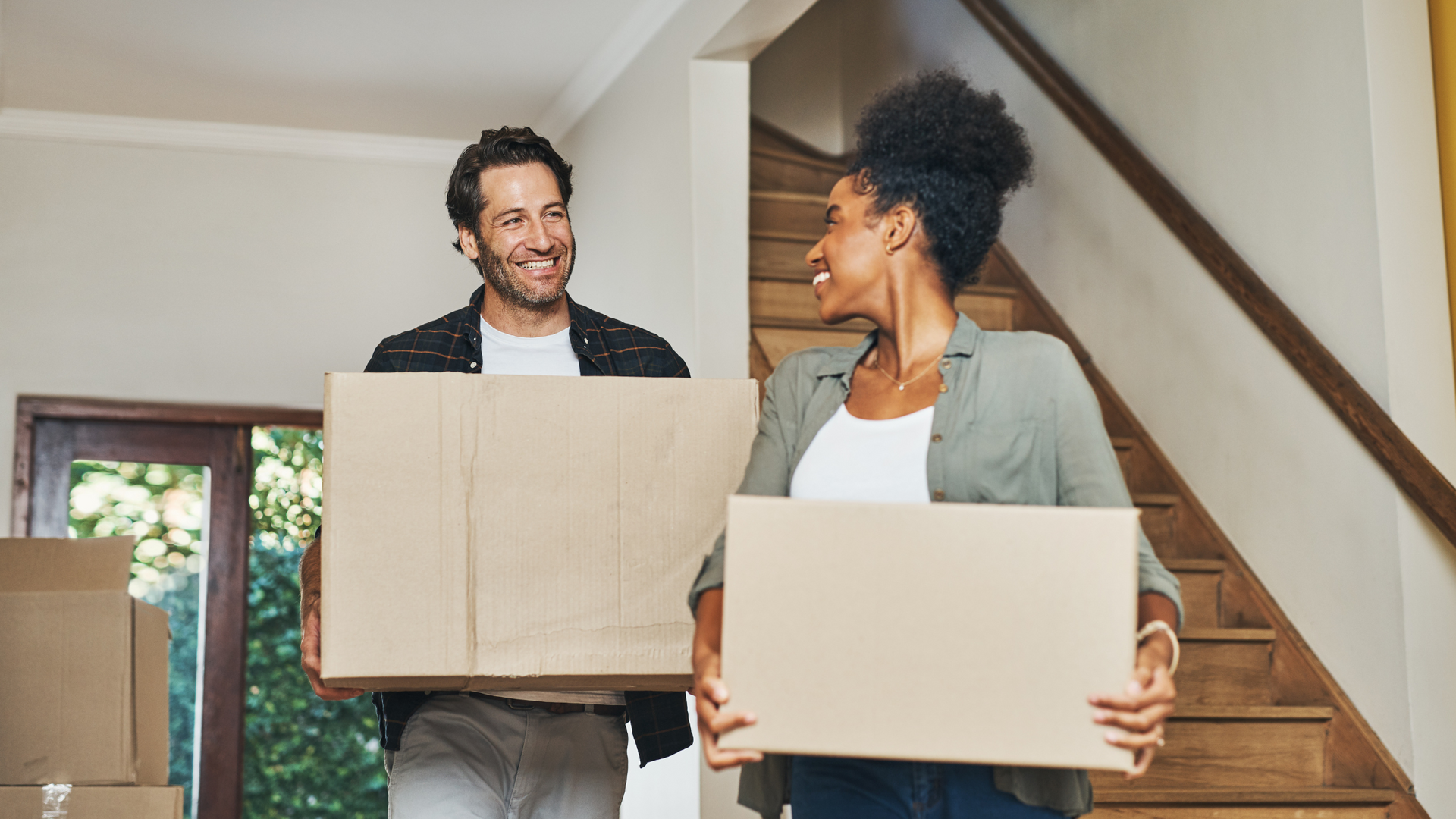 a man and a woman are holding cardboard boxes in their new home .