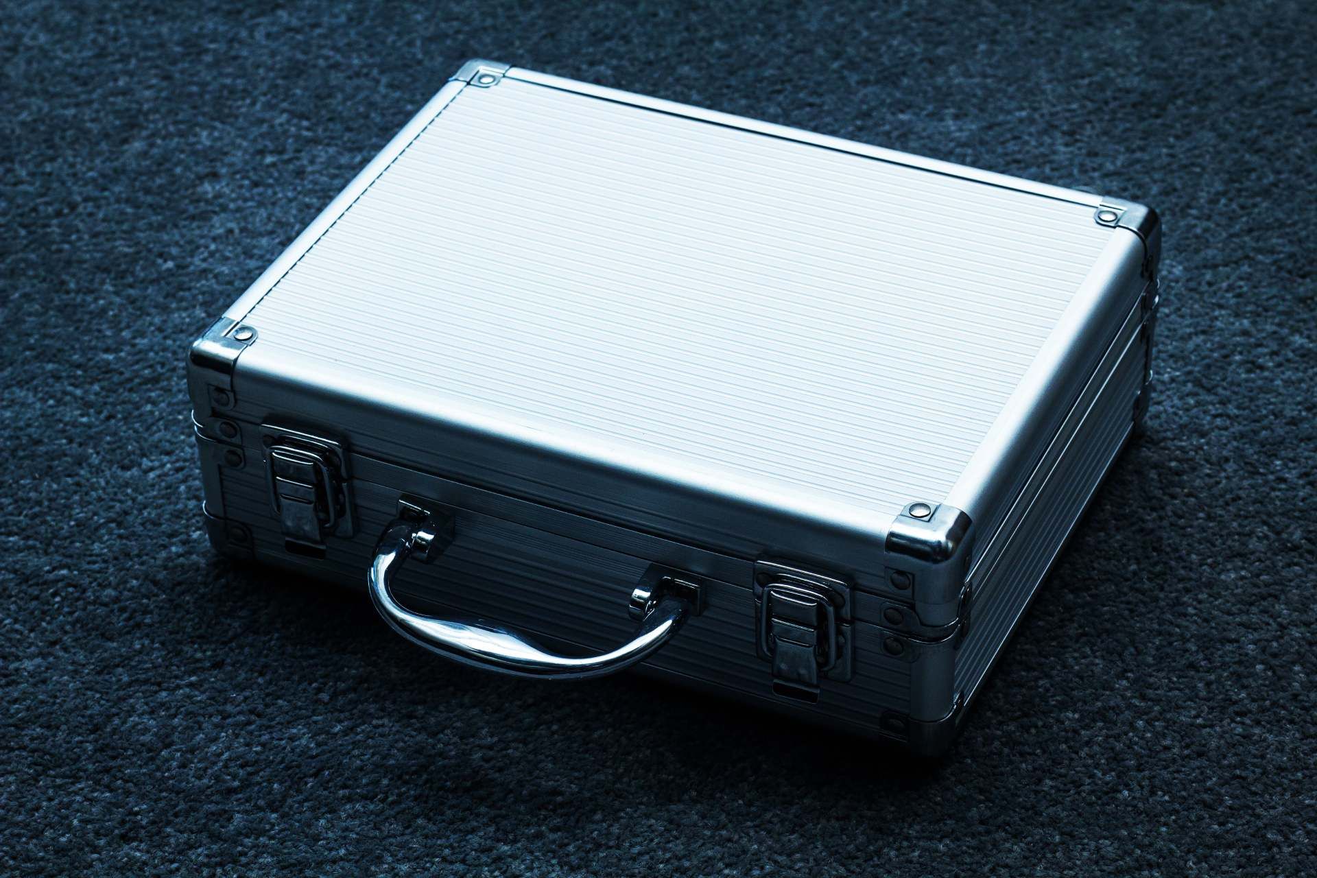 A silver briefcase is sitting on a black carpet.
