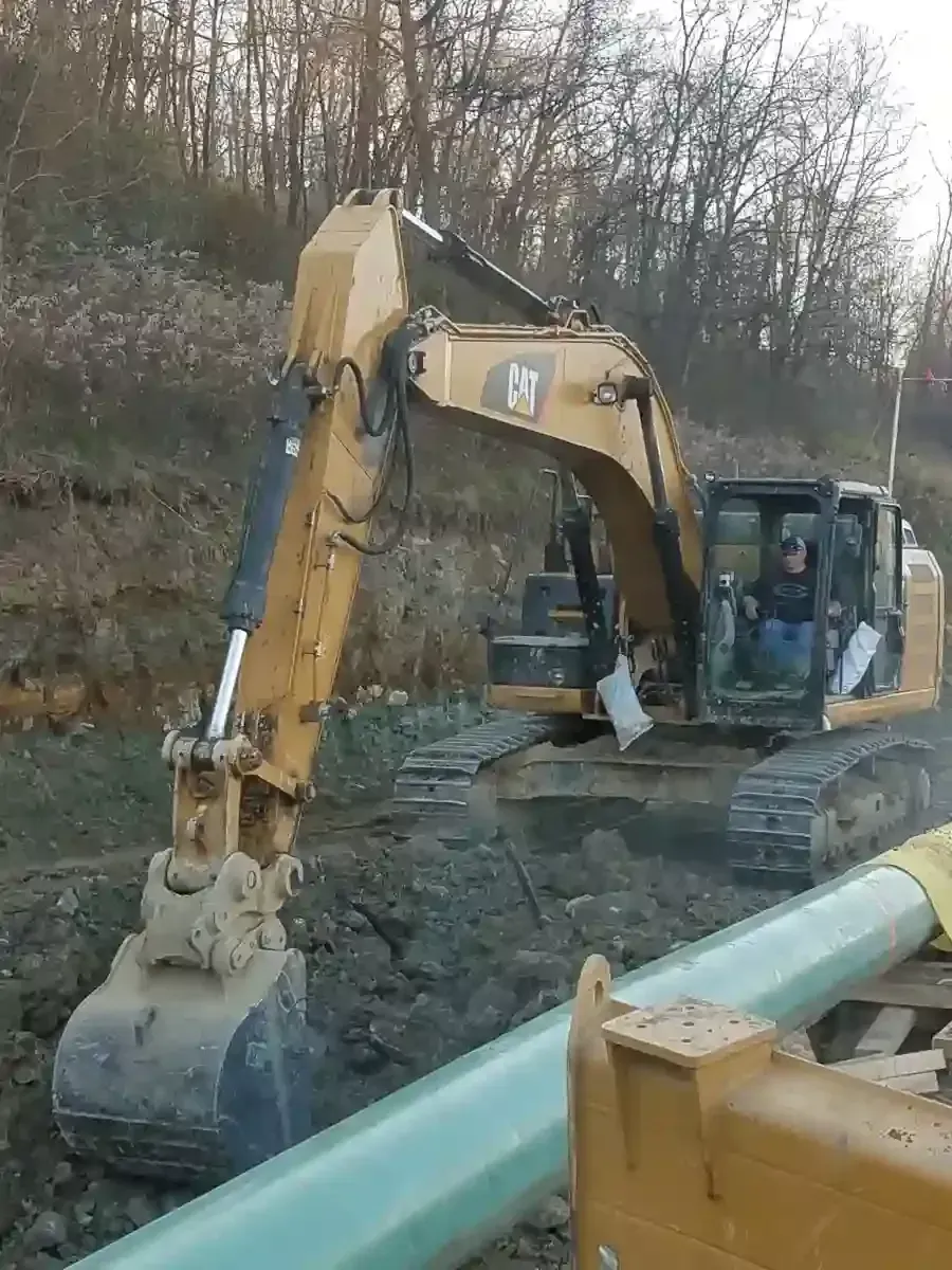 A yellow John Deere 85G excavator sits on a dirt mound at a construction site.
