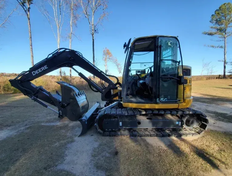 A yellow excavator moves dirt on a hillside under a clear blue sky.