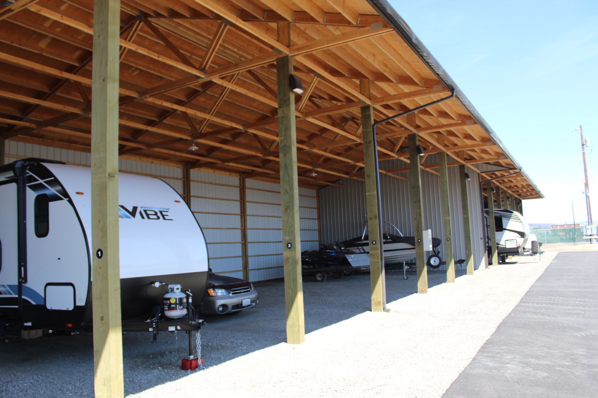 RV storage facility with covered parking spaces. RVs, boats, and cars parked under wooden structures.
