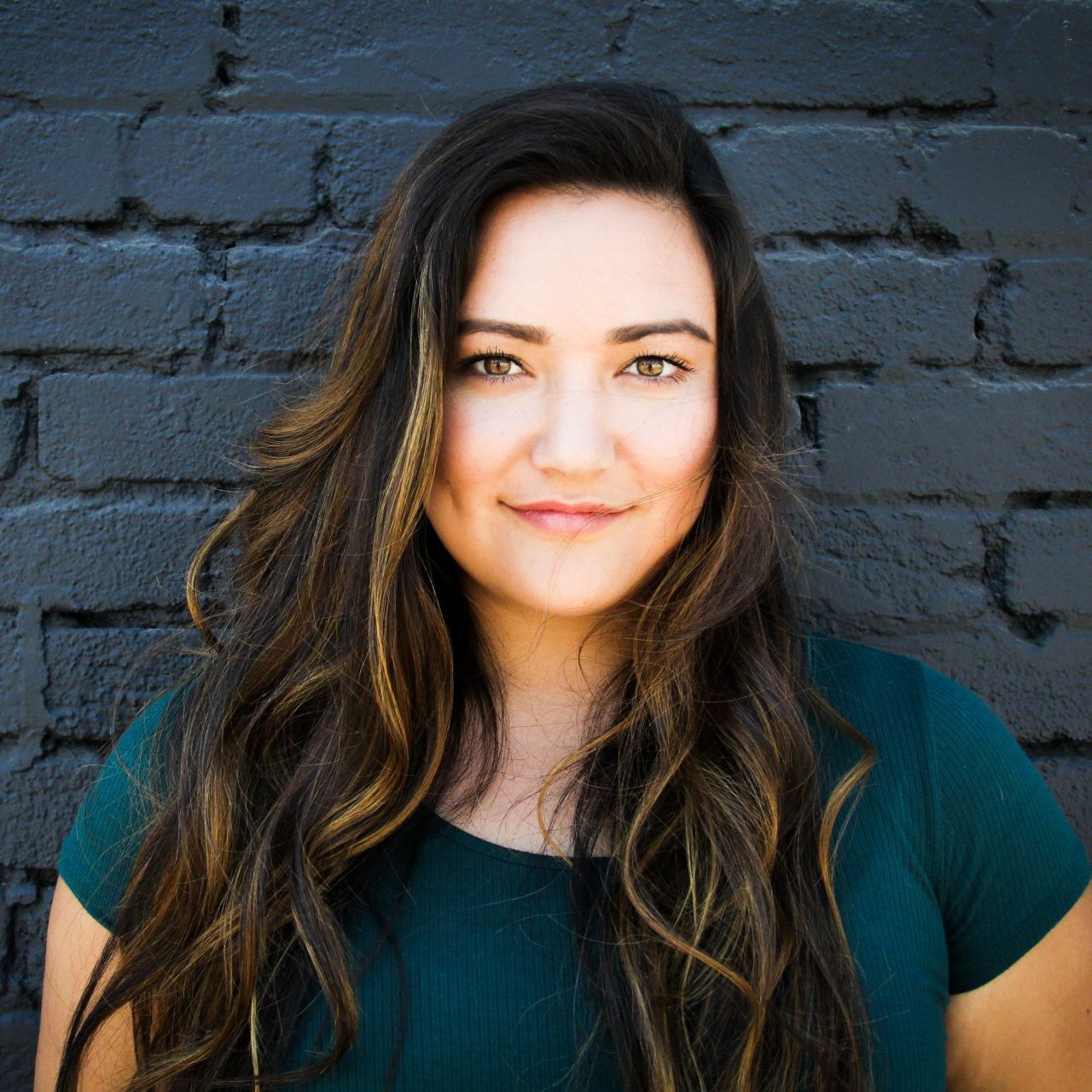 A woman with long hair is standing in front of a brick wall.