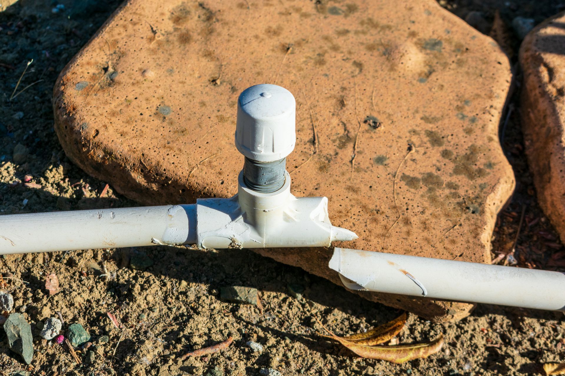 A white pipe is sitting on top of a rock on the ground.