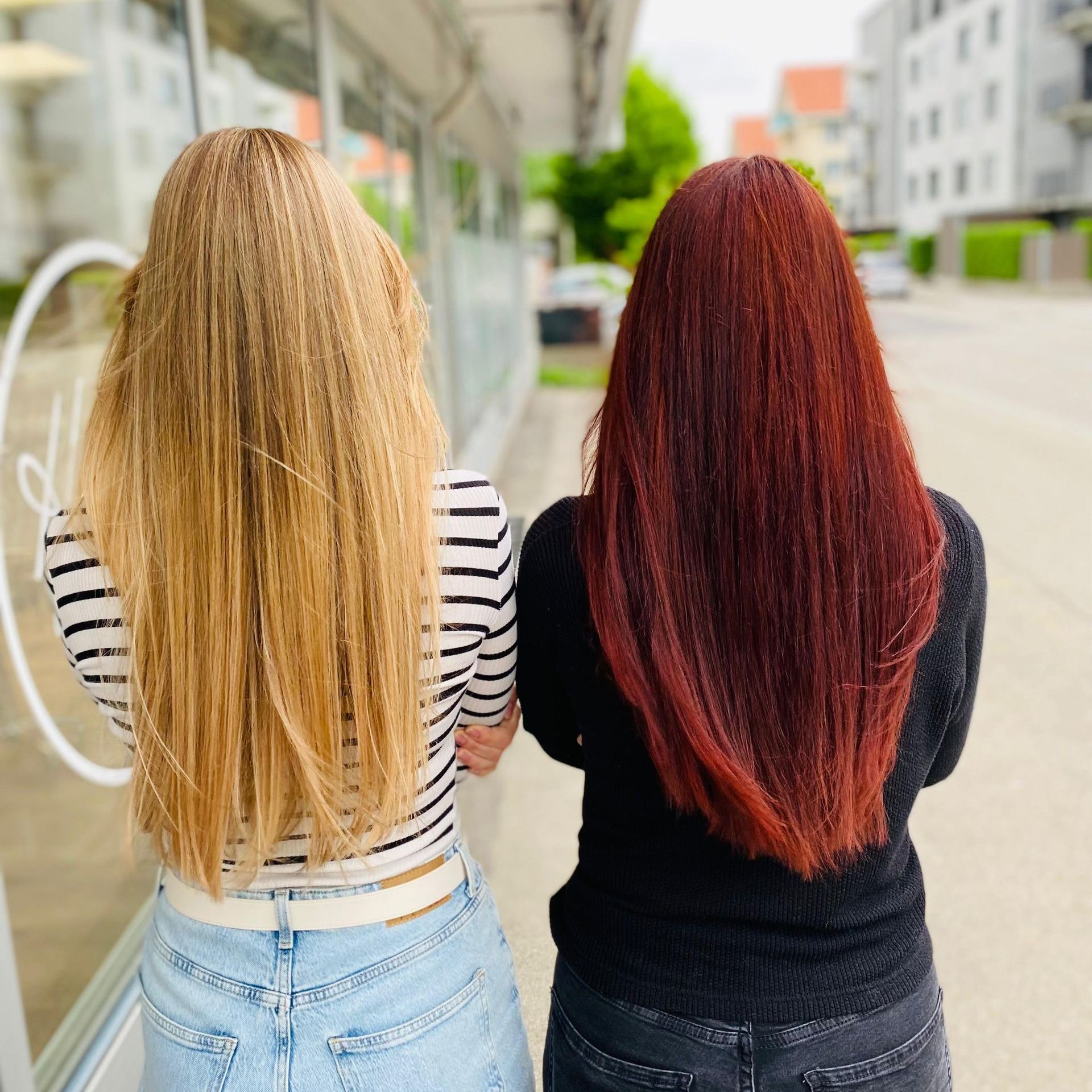 Frisch vom Coiffeur.
Zwei Frauen gehen auf einem Bürgersteig; eine mit blondem, gewelltem Haar, die andere mit rotem Haar.