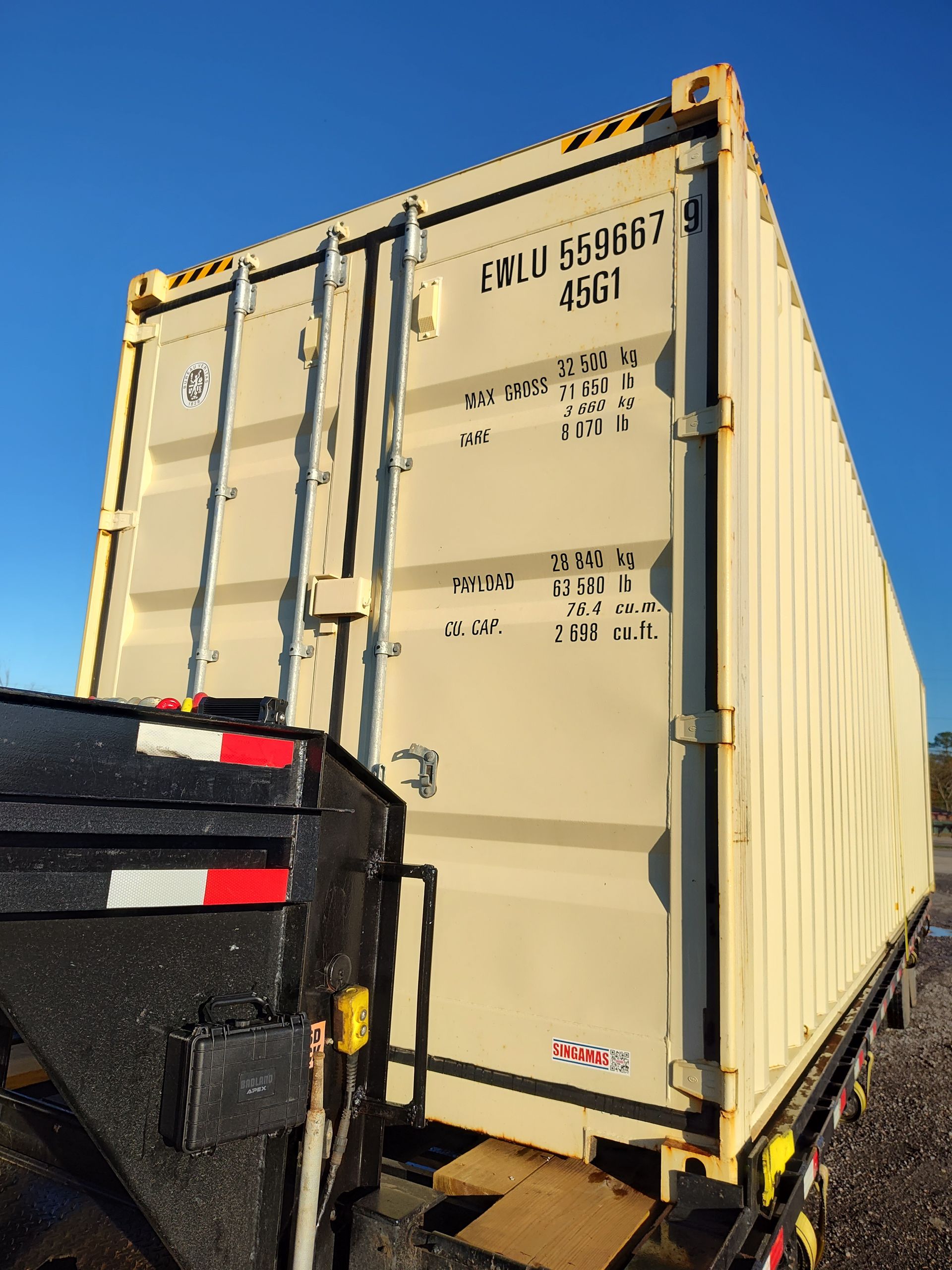 A yellow semi truck is driving down a highway next to a row of shipping containers.