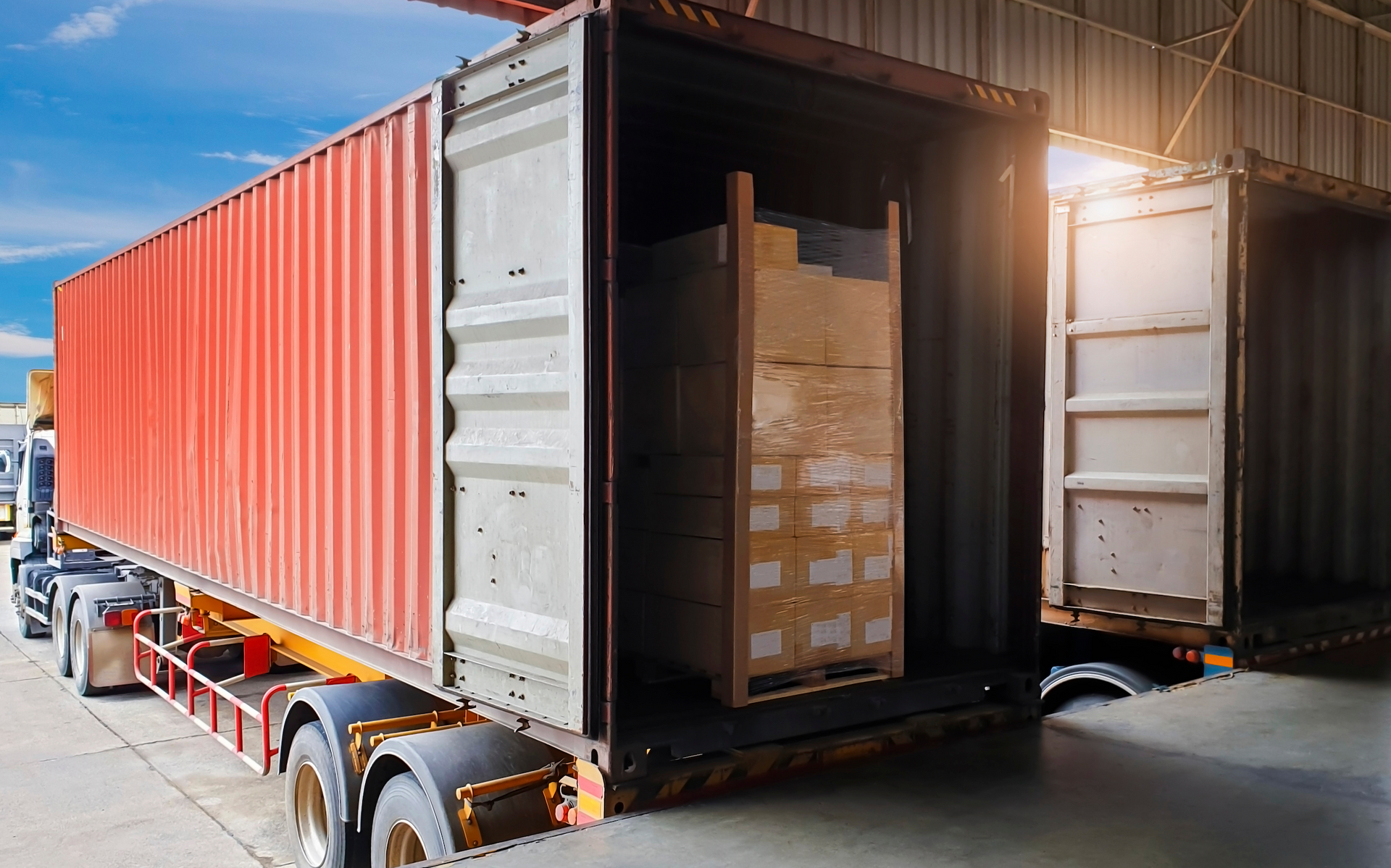 Two shipping containers are being loaded with boxes in a warehouse.
