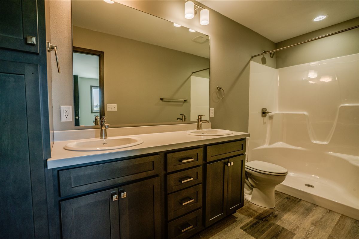 A bathroom featuring a dark wood vanity with dual sinks, a large mirror, and a walk-in shower with a toilet nearby.