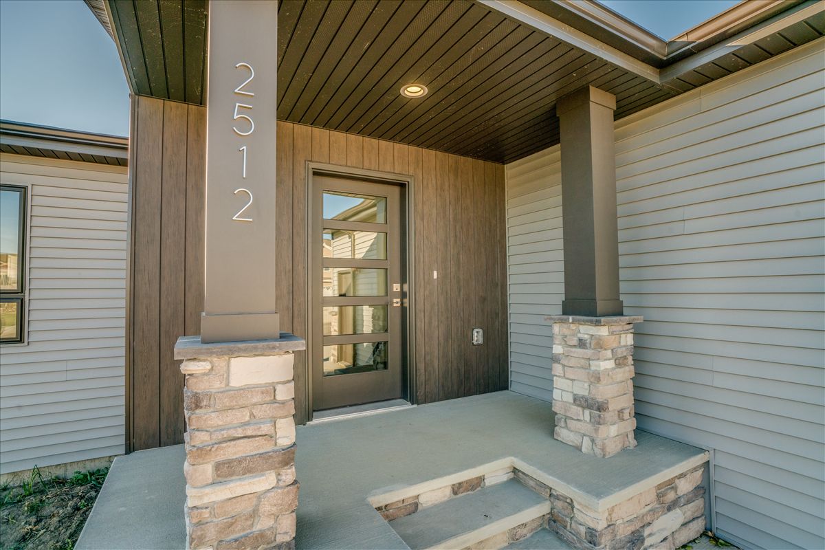 A modern home entrance with a dark wood door, two stone-based columns, and light gray siding under a covered porch.