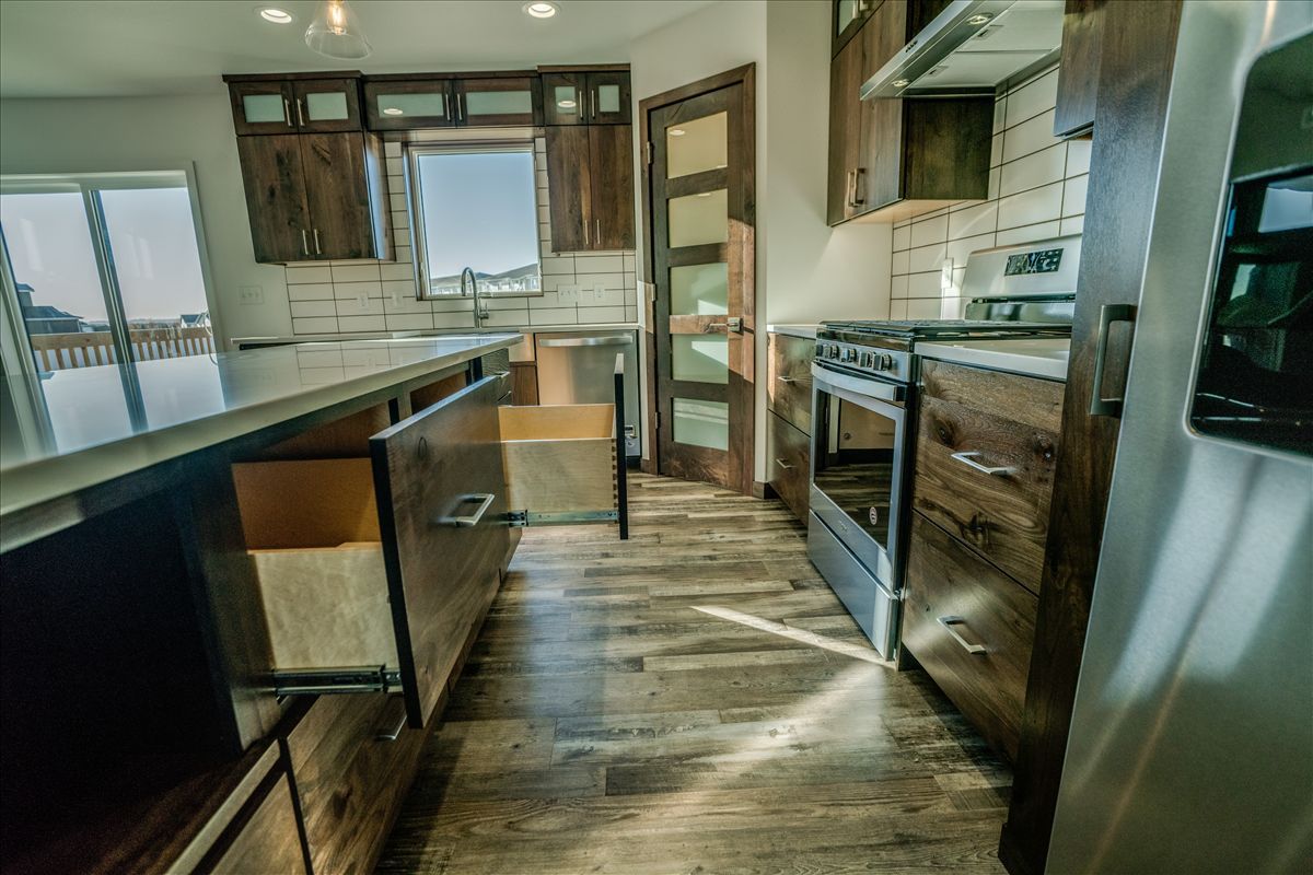 Modern kitchen interior with dark wood cabinets, a large island with an open drawer, a stainless stove, and wood flooring.