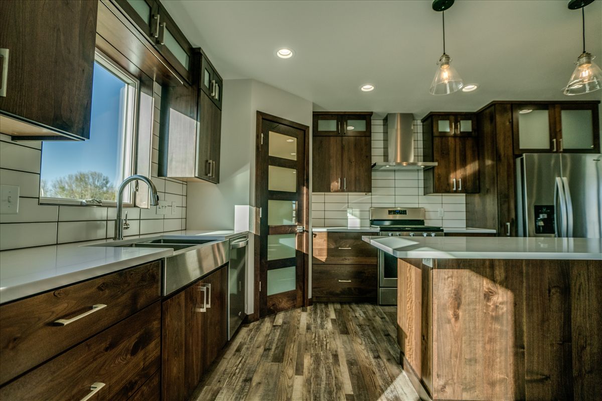 A rustic kitchen featuring dark wood cabinets, white subway tile backsplash, stainless steel appliances, and a wood floor.