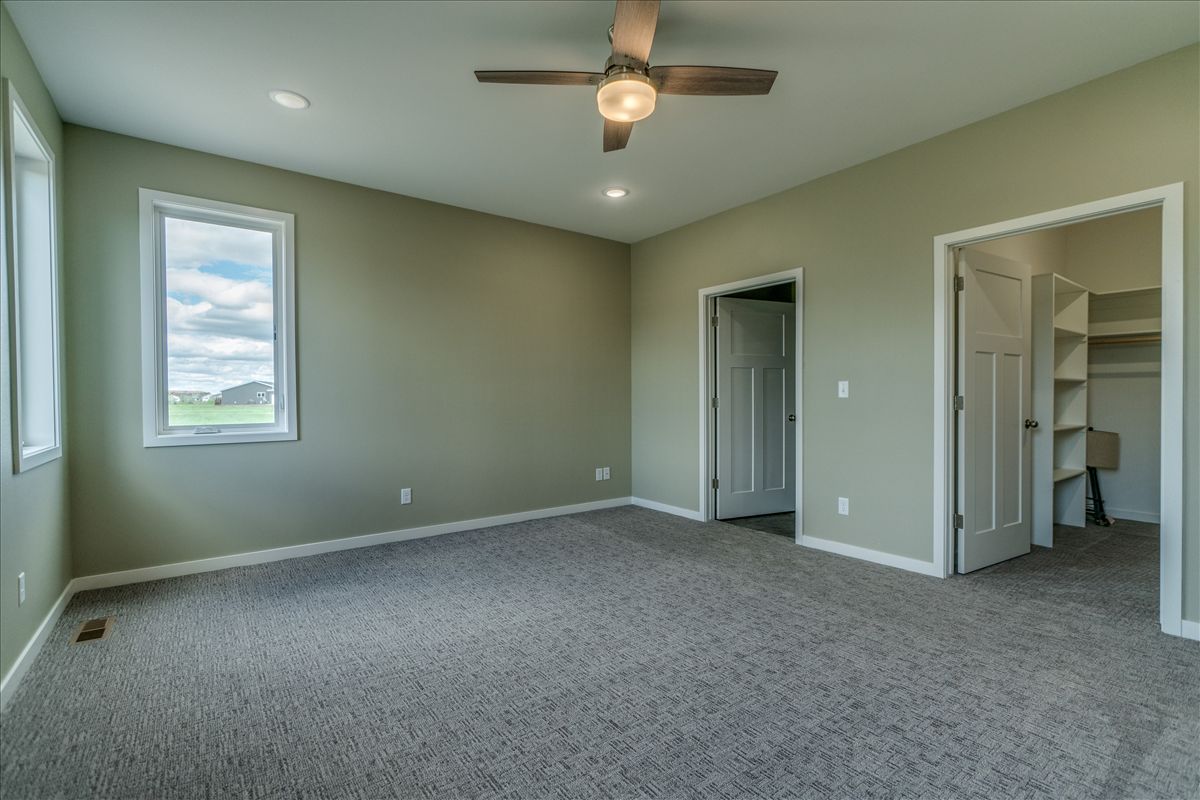 Empty room with light sage walls, gray carpet, ceiling fan, a window, and two doorways leading to a closet and hallway.