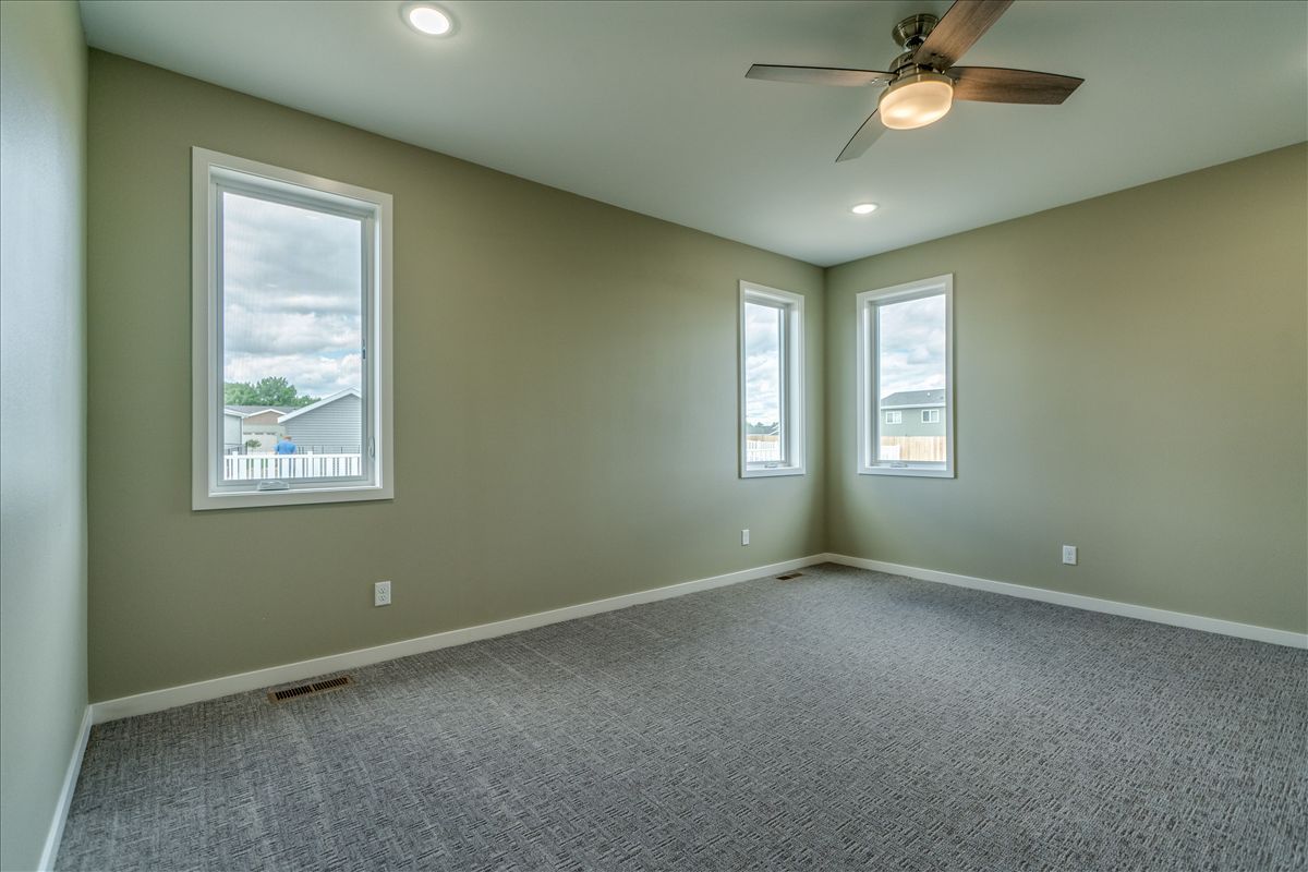 A vacant bedroom with sage green walls, gray carpet, two windows, and a ceiling fan.
