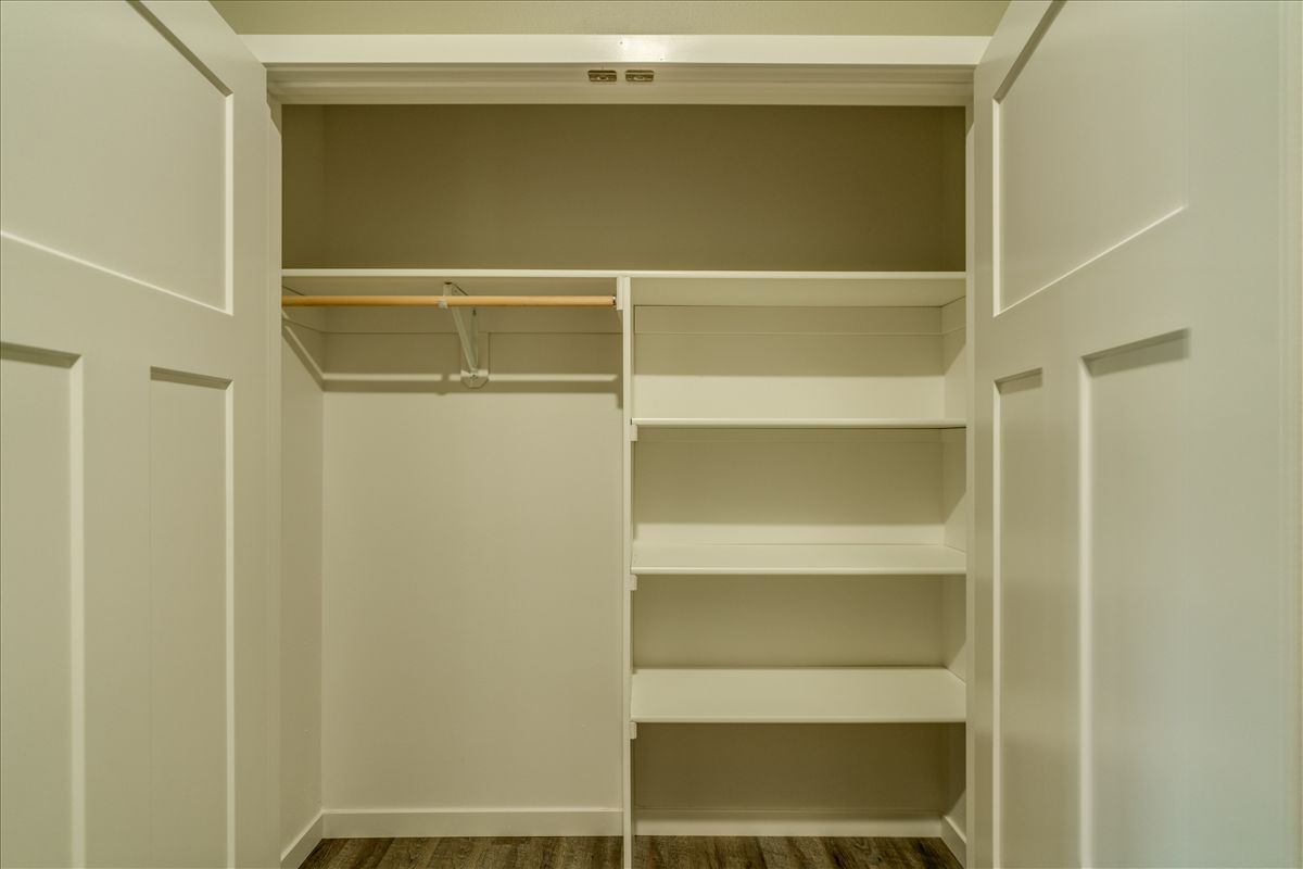 A closet with white double doors open to reveal a hanging rod on the left and white shelving on the right.