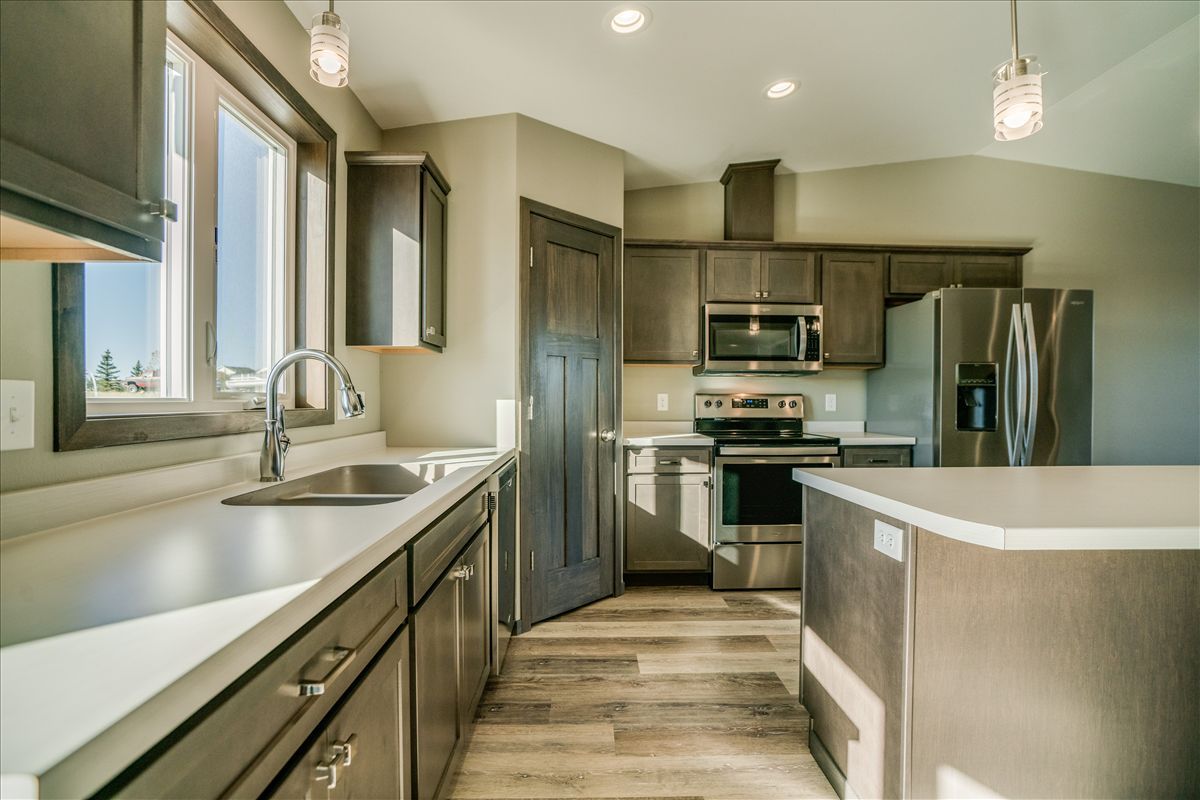 Modern kitchen with dark wood cabinets, stainless steel appliances, white countertops, and wood-look laminate flooring.