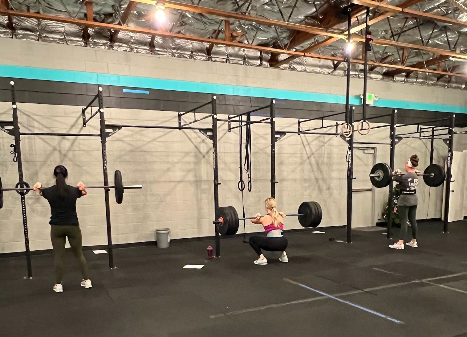 A group of people are squatting with barbells in a gym.