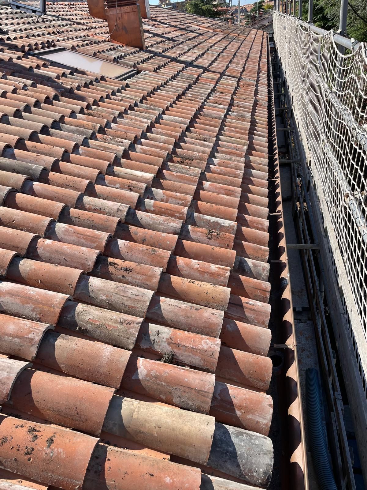 Tetto in tegole di argilla rossa con rete di sicurezza lungo un bordo.