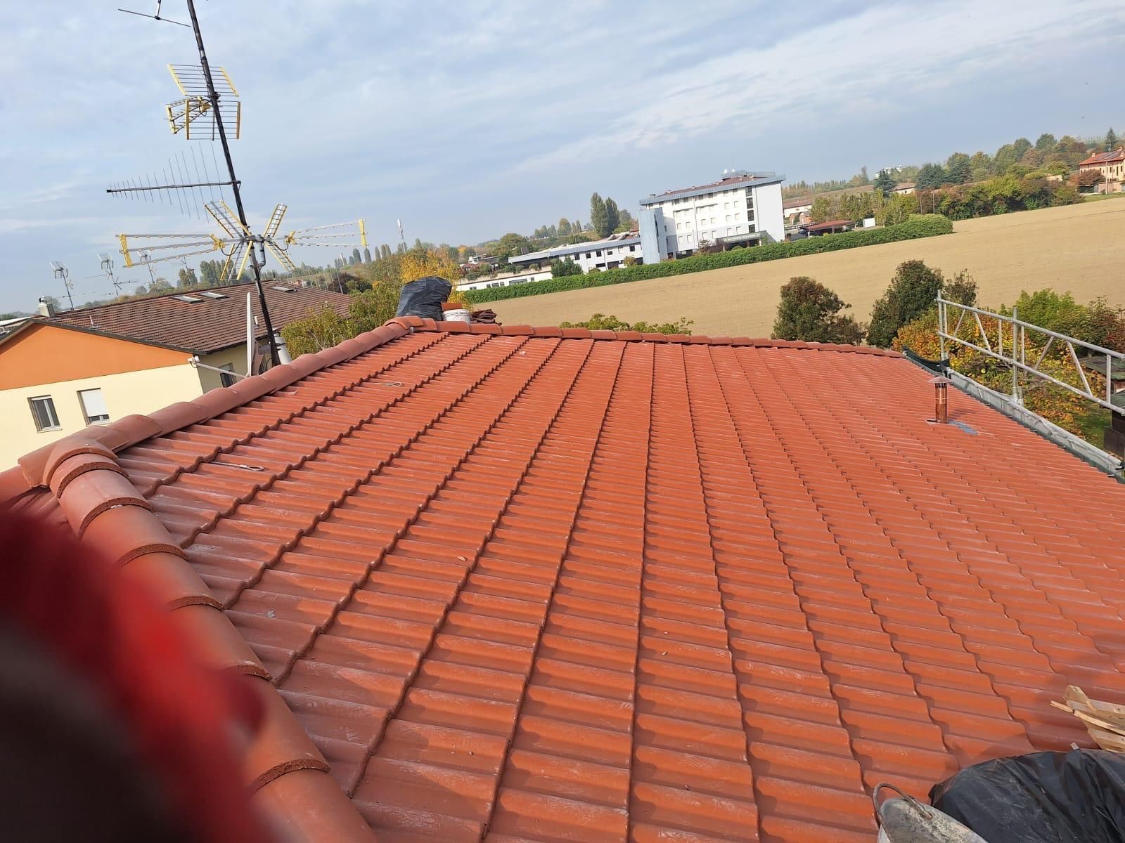 Tetto di tegole rosse di un edificio, vista aerea. Antenna visibile, cielo nuvoloso, sfondo rurale.