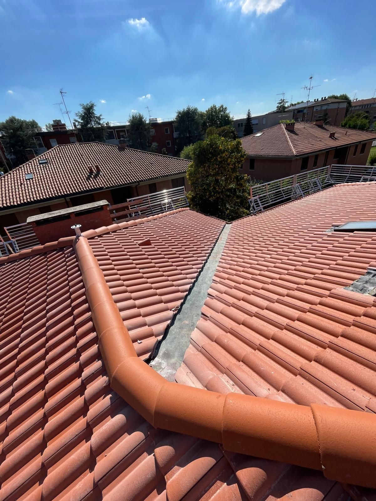 Tetti di tegole rosse con grondaie arancioni contro un cielo blu.