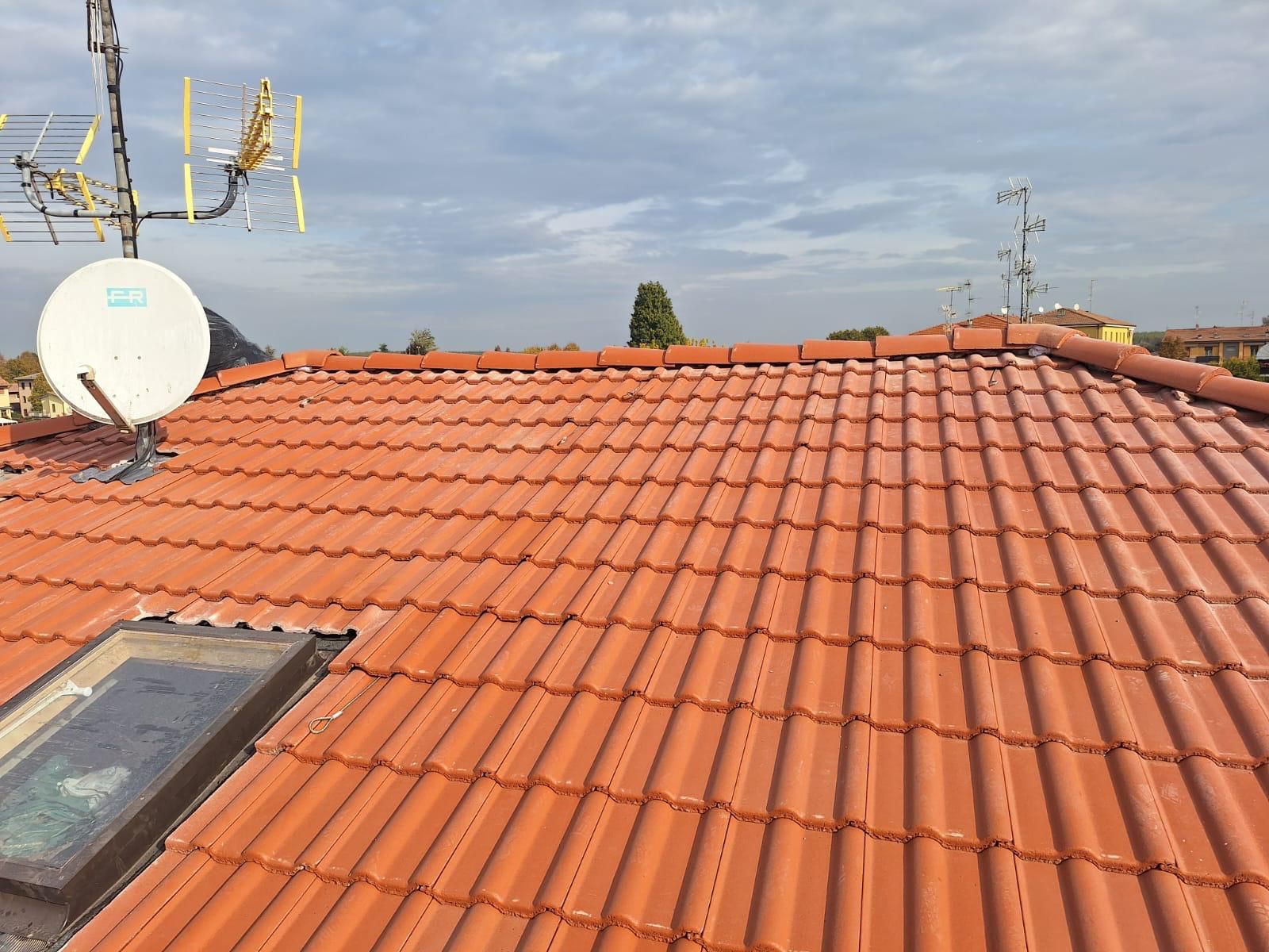 Tetto di tegole rosse con antenne e parabola satellitare sullo sfondo di un cielo nuvoloso.