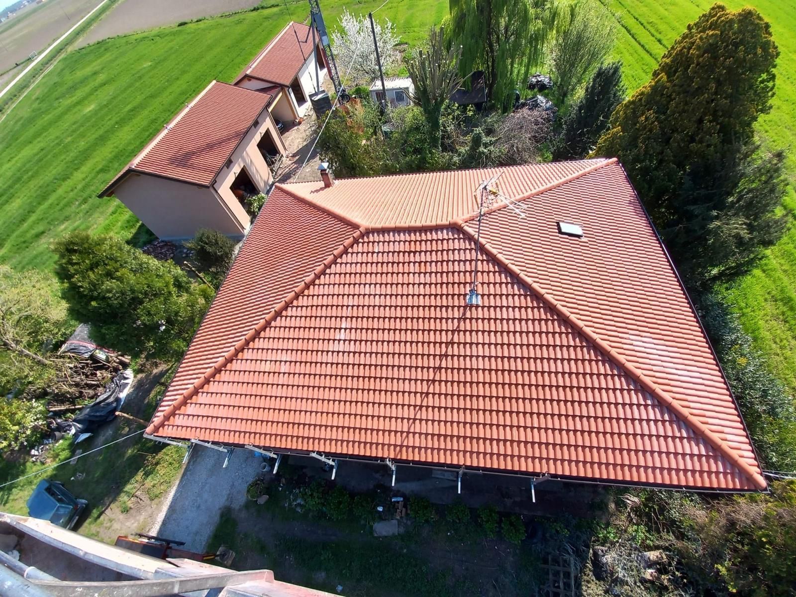 Vista dall'alto del tetto in tegole di terracotta di un edificio, circondato da campi verdi e alberi.