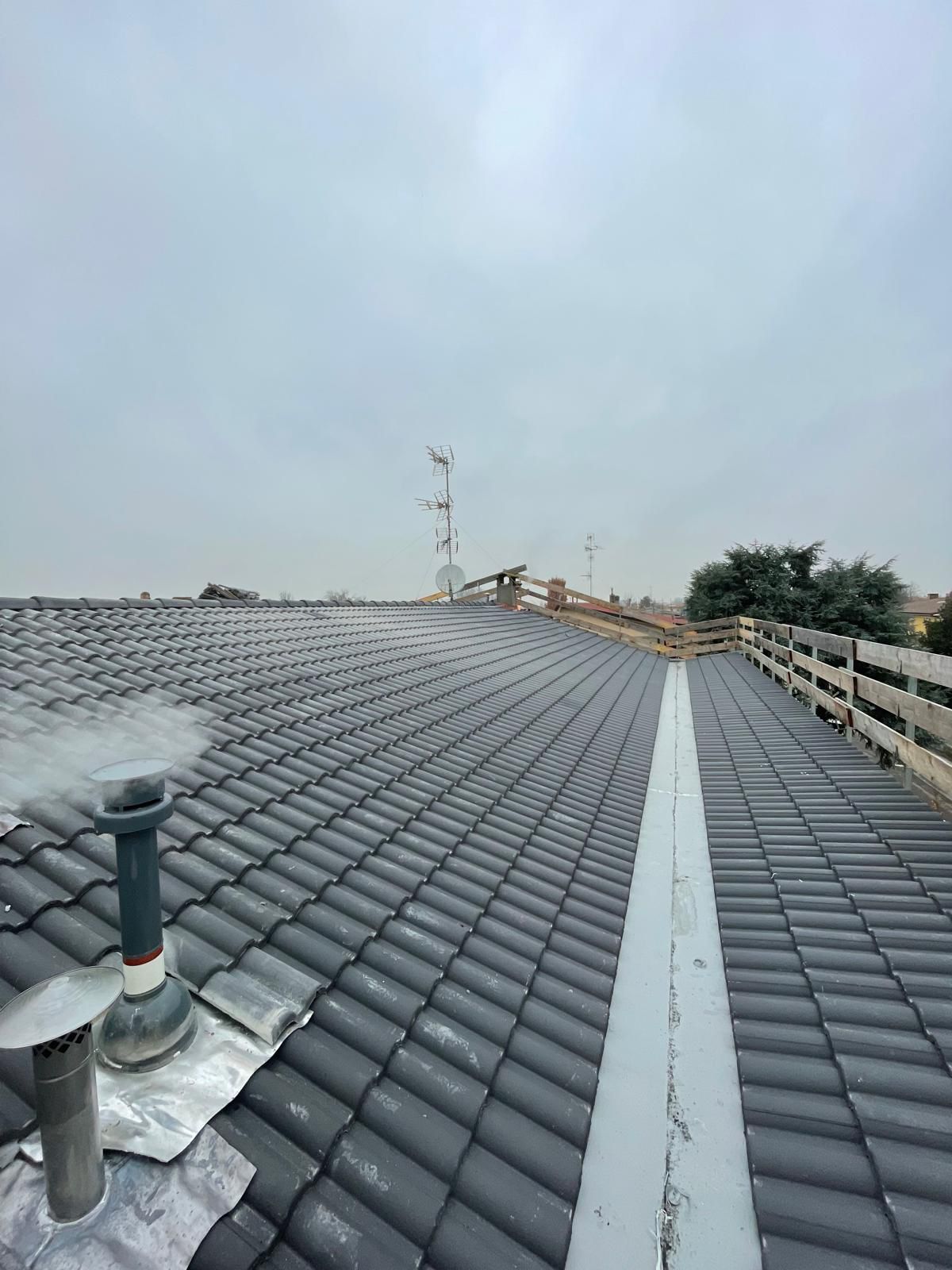 Tetto in tegole grigie con ringhiera di sicurezza e sfiato, cielo coperto.