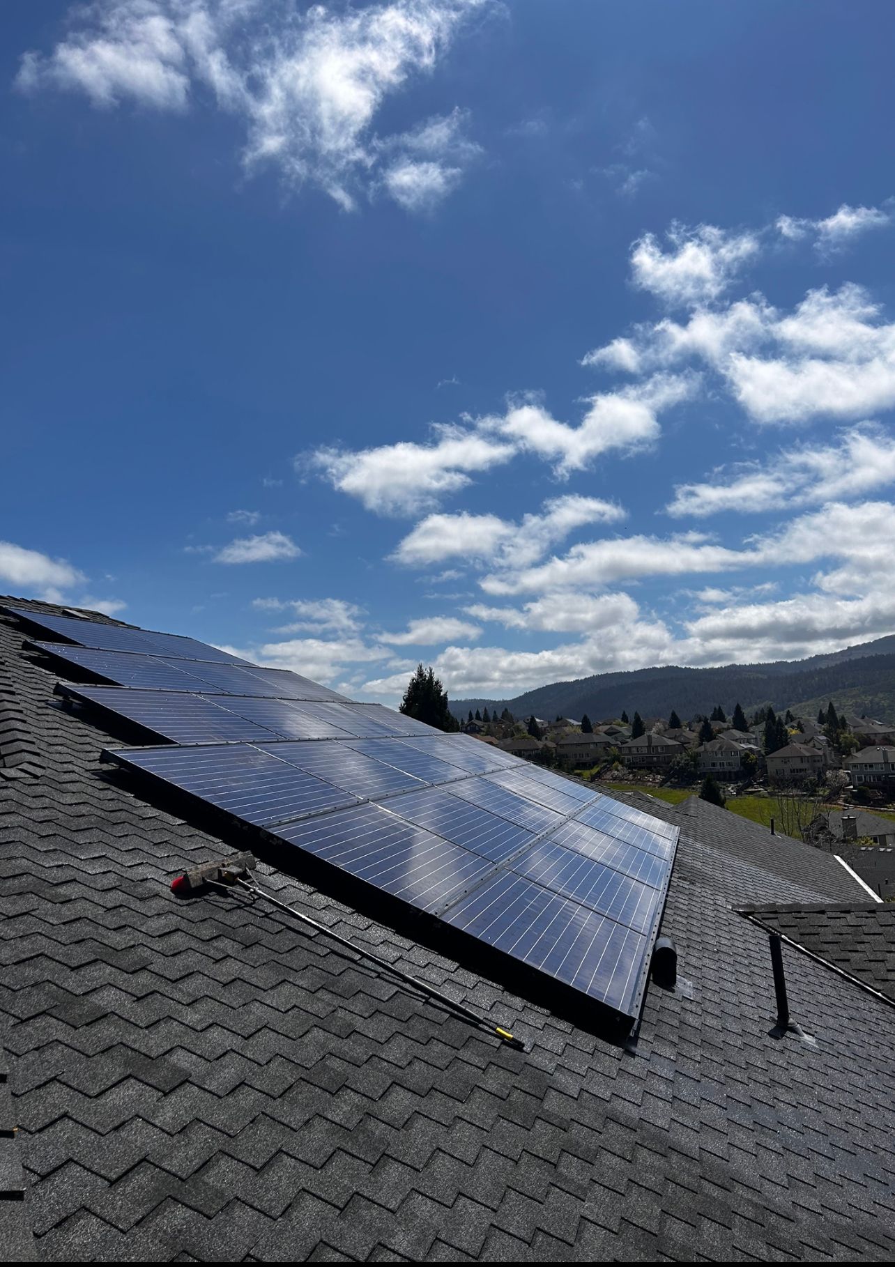 Solar panels on a sloped roof under a partly cloudy blue sky. Mountains in the distance.