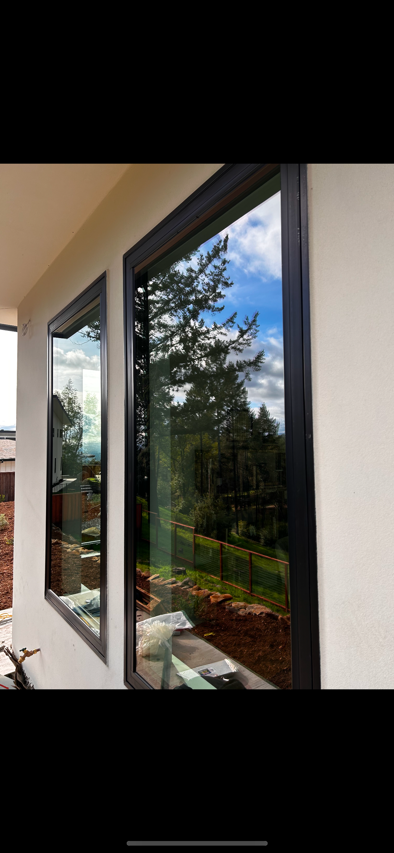 Two black-framed windows reflect trees and sky on a white building exterior.