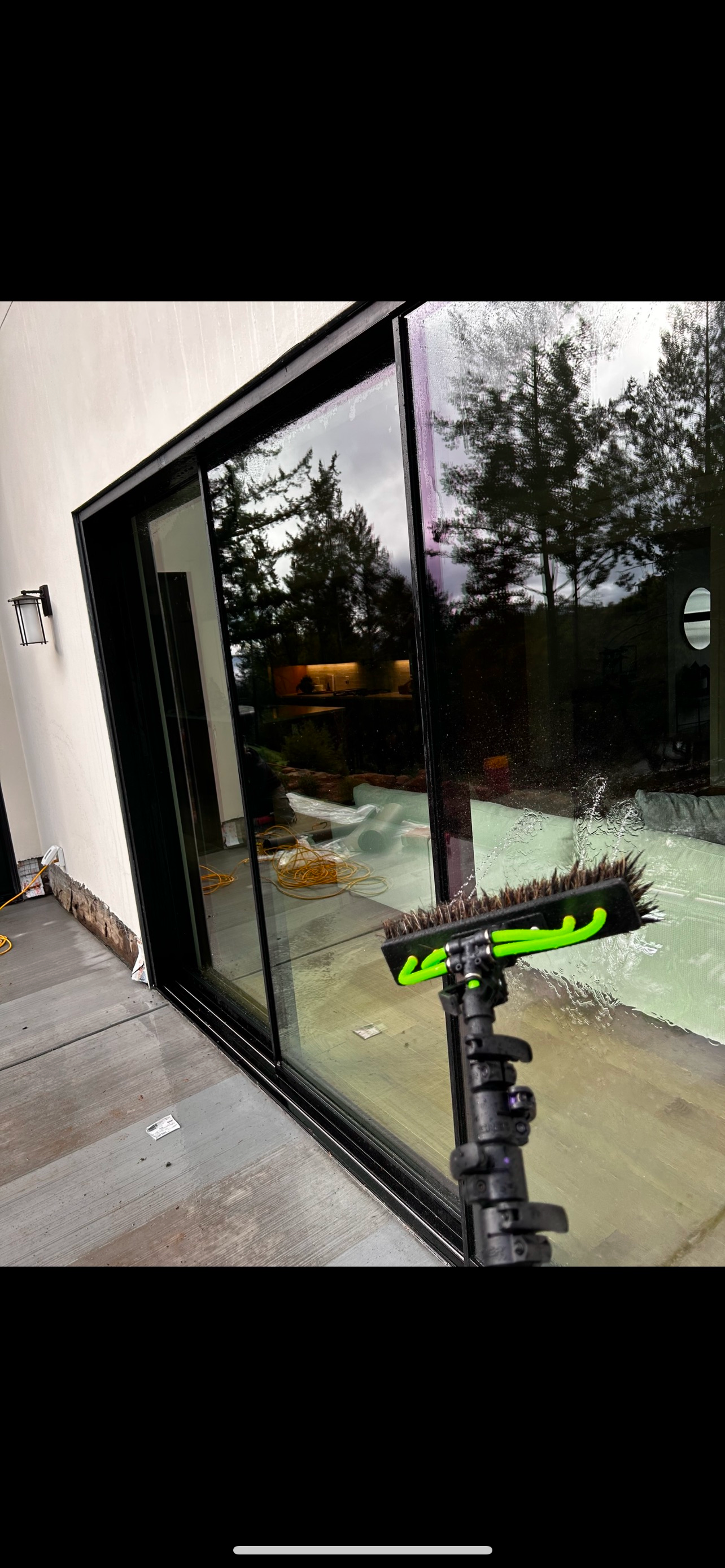 Window being cleaned with a brush on a pole; reflections of trees and buildings are visible.