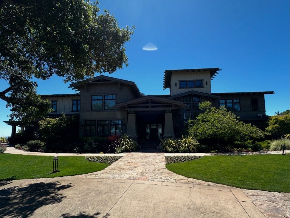 Large, multi-story house with stone driveway and landscaped yard under a clear blue sky.