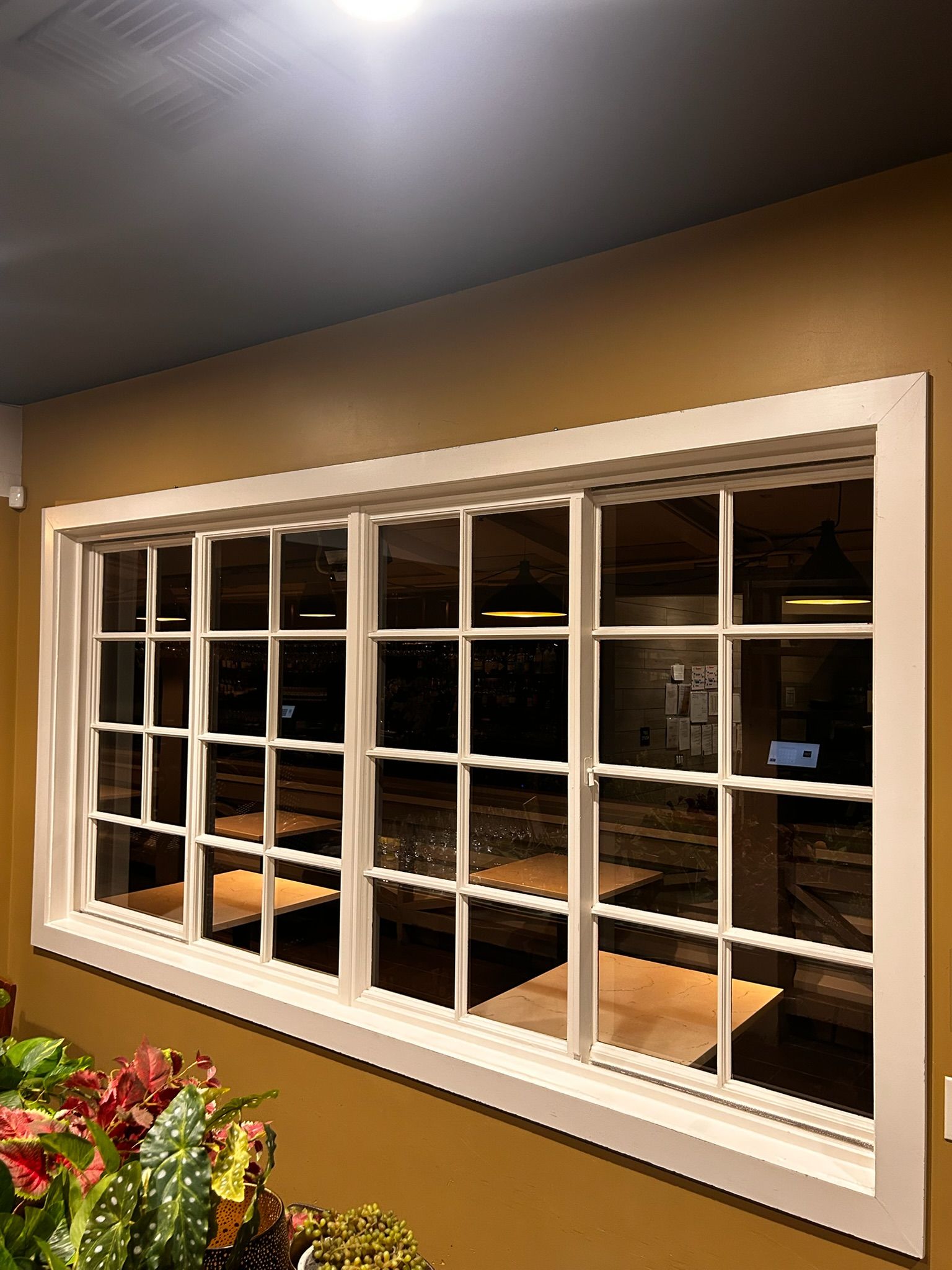 White-framed window with grid, reflecting a nighttime street scene, on a tan wall.