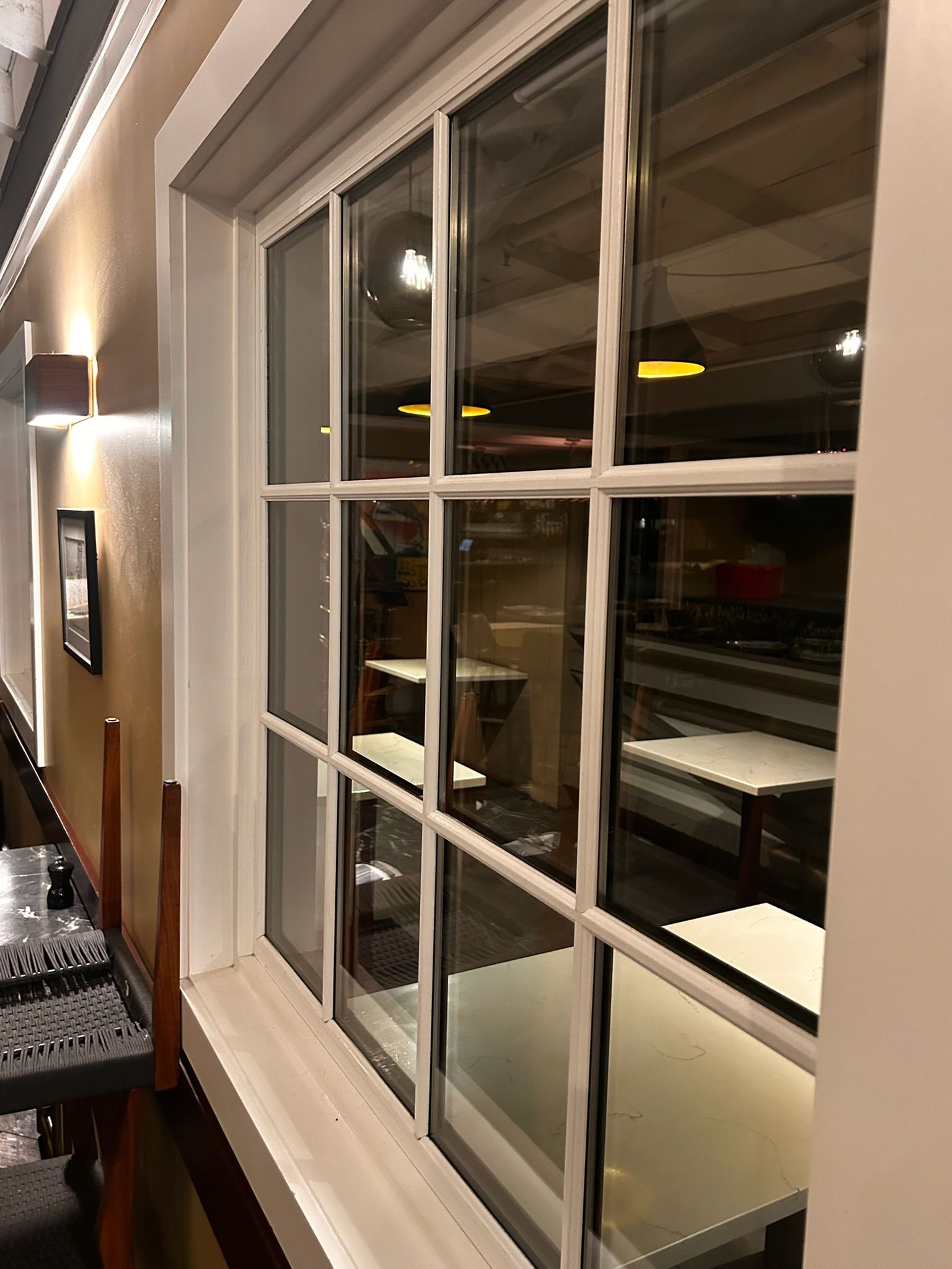 White-framed window with multiple panes reflecting an interior space with tables and a bar.