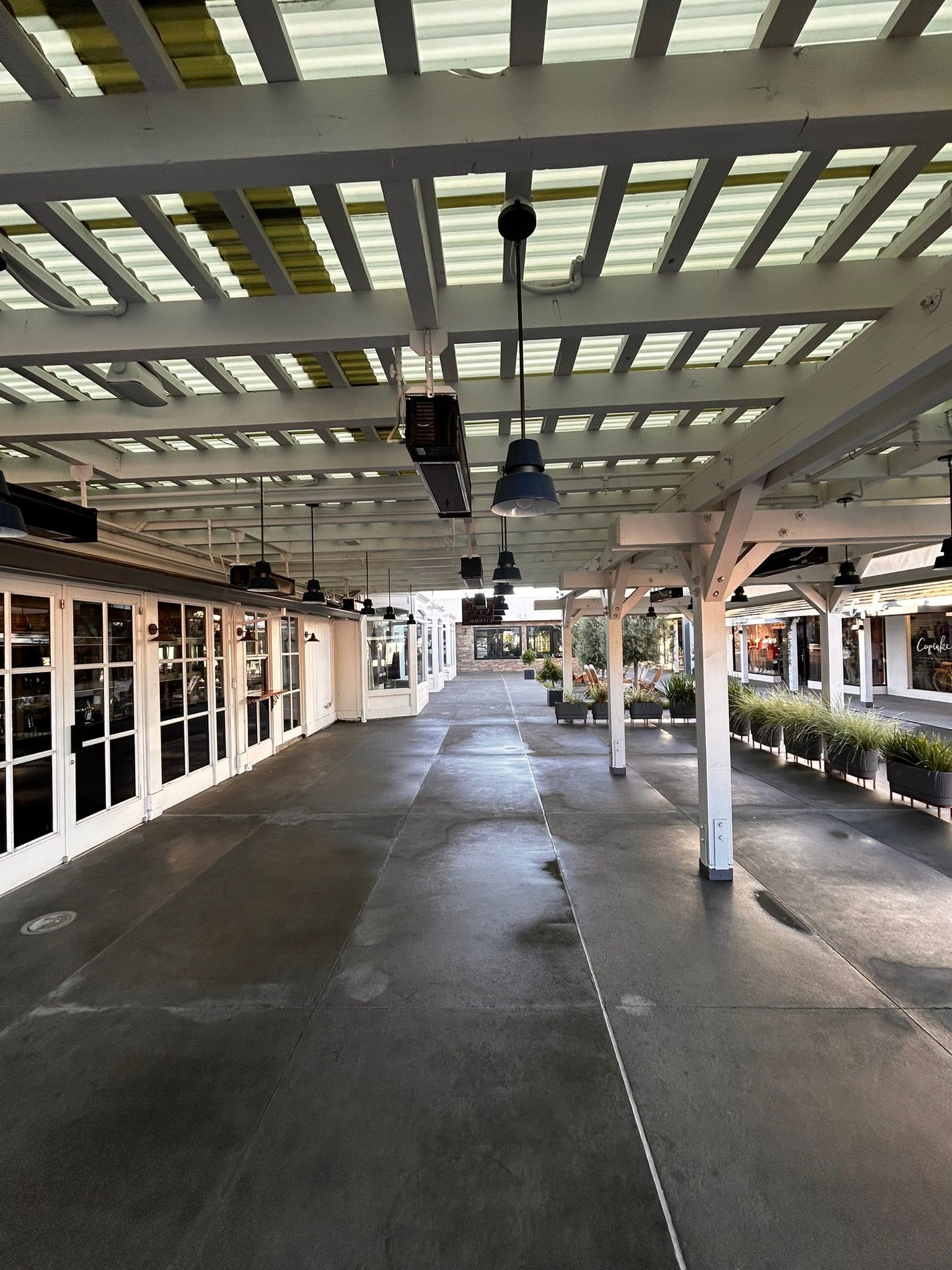 Covered outdoor walkway with white pergola roof. Restaurants with glass doors line the sides.