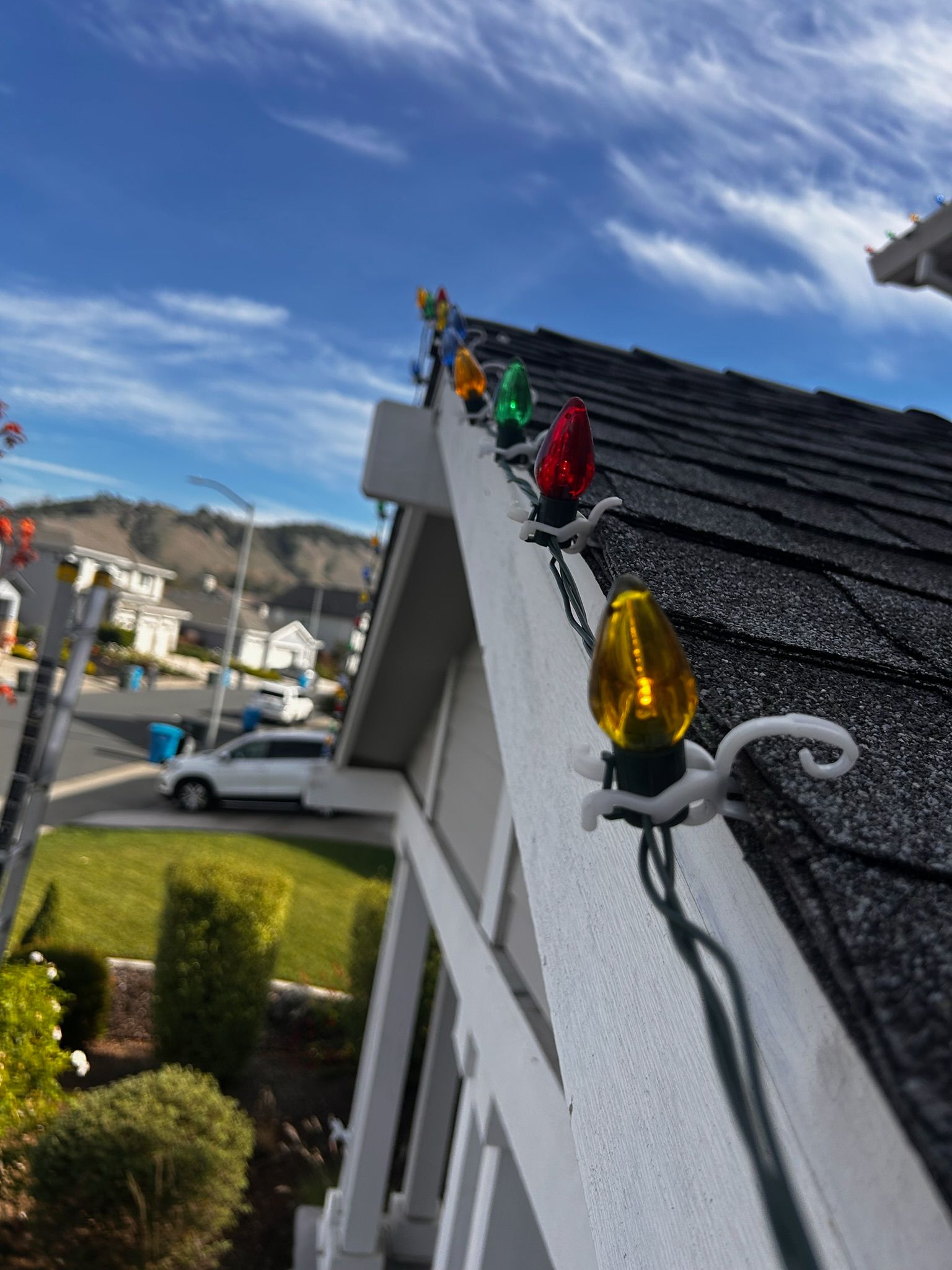 Christmas lights on a roof's edge against a blue sky, illuminating the day.